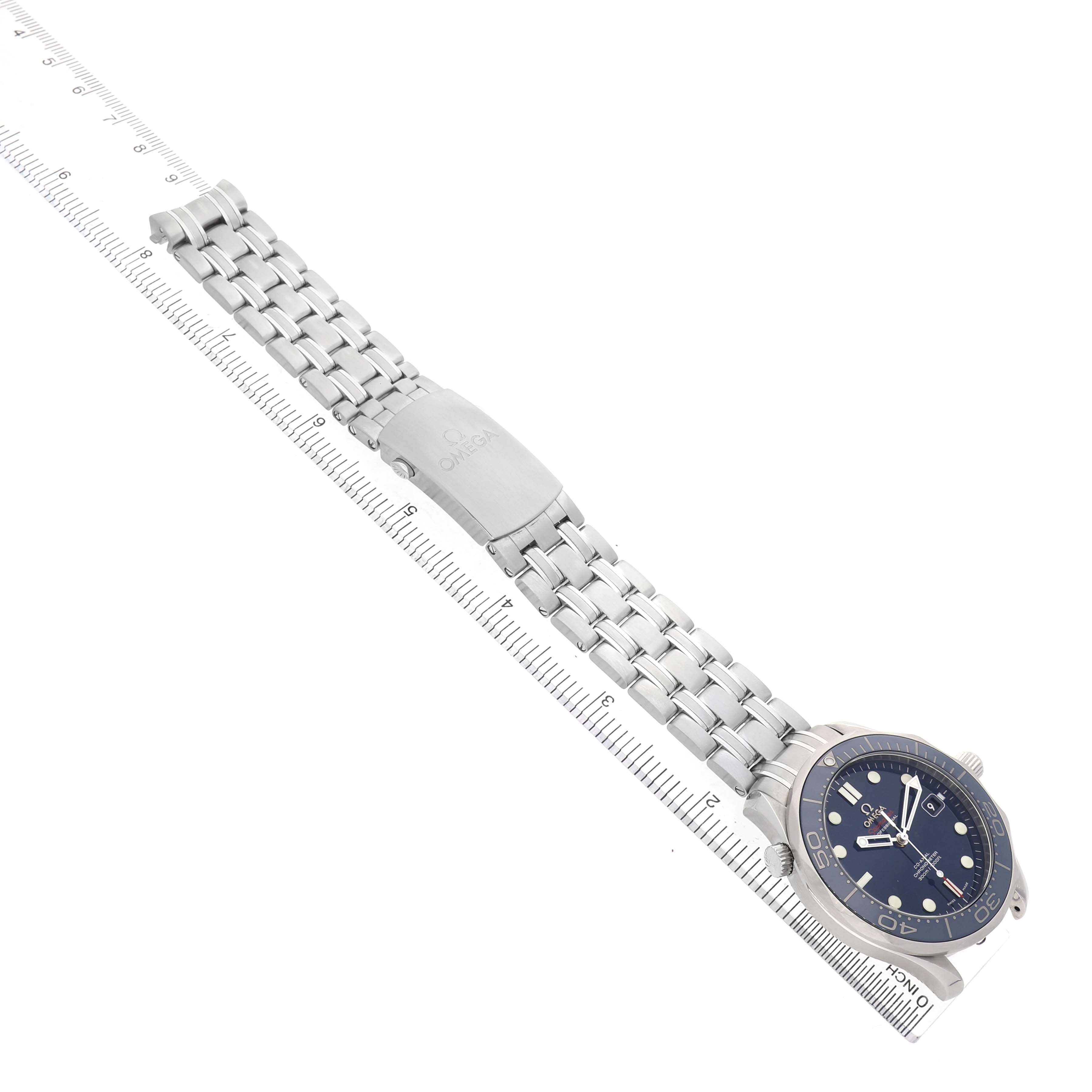 The Omega Seamaster 212.30.41.20.03.001 Men's Stainless Steel Blue Dial watch is shown from an angled side view, highlighting the band, clasp, and face on a ruler.