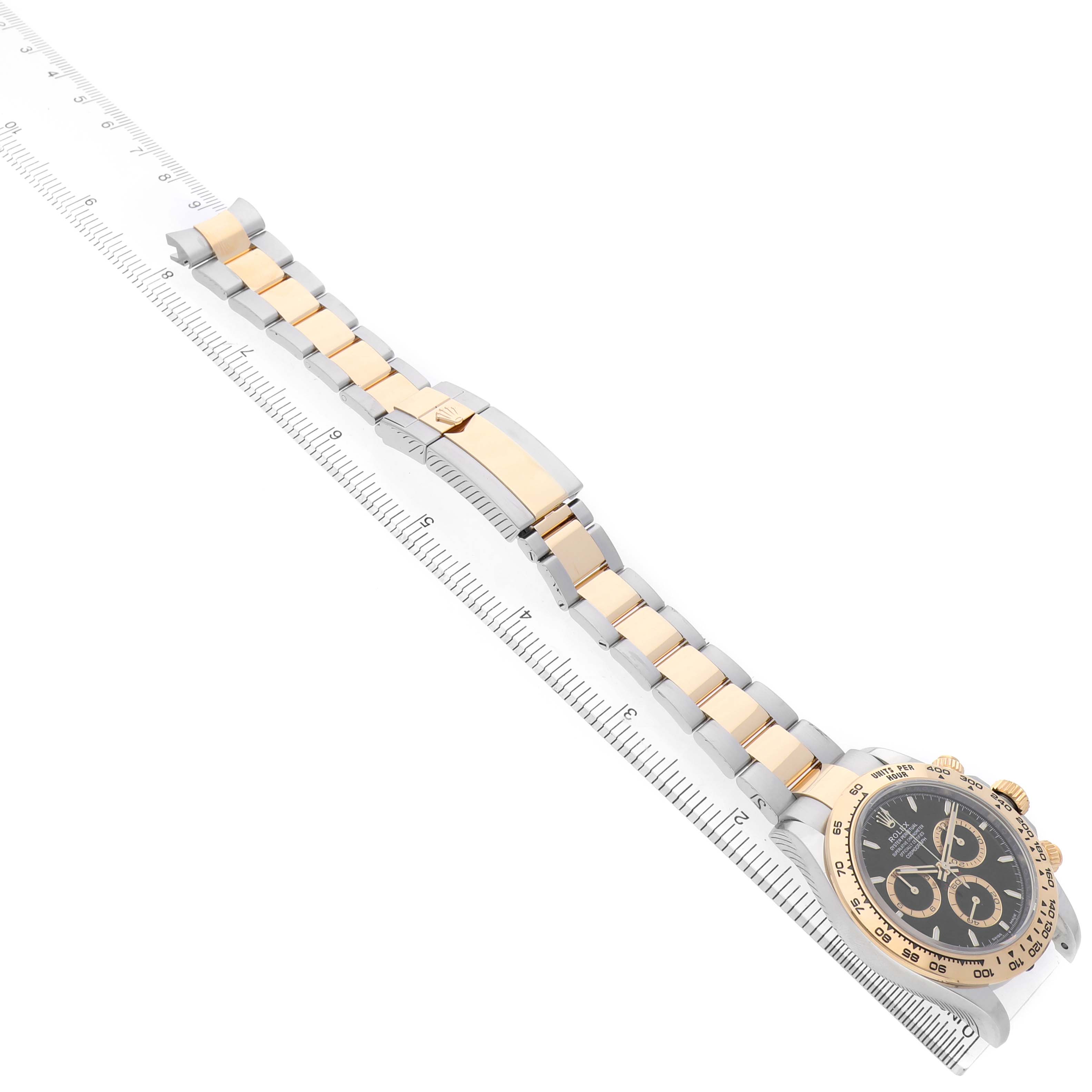 The Rolex Daytona 126503 Men's Steel and Gold (two tone) Black Dial watch is displayed from a top angle, showing the face, bezel, and full bracelet on a ruler.
