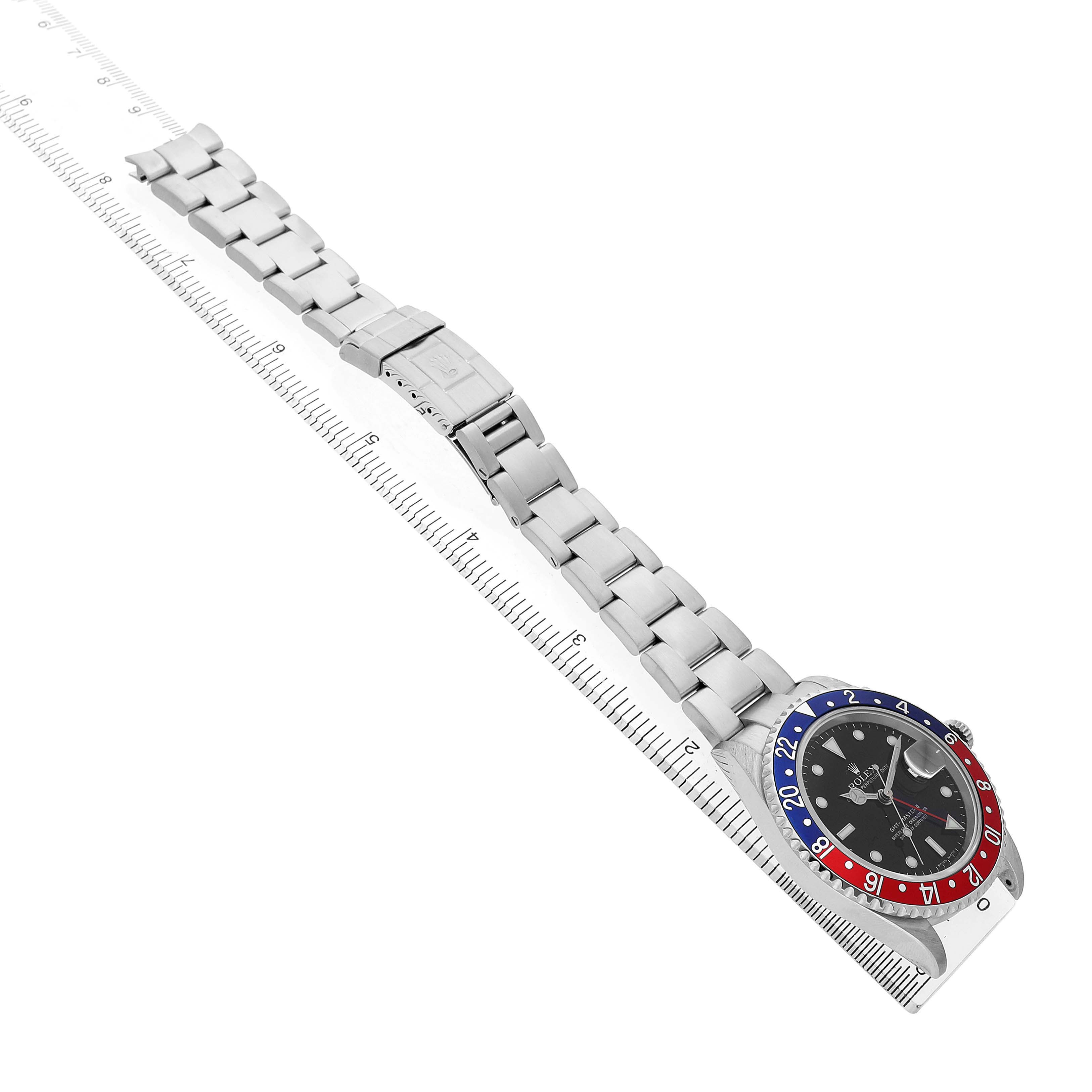 The Rolex GMT-Master 16710 Men's Stainless Steel Black Dial watch is shown from a top-down angle, displaying the entire bracelet and face, laid alongside a ruler.