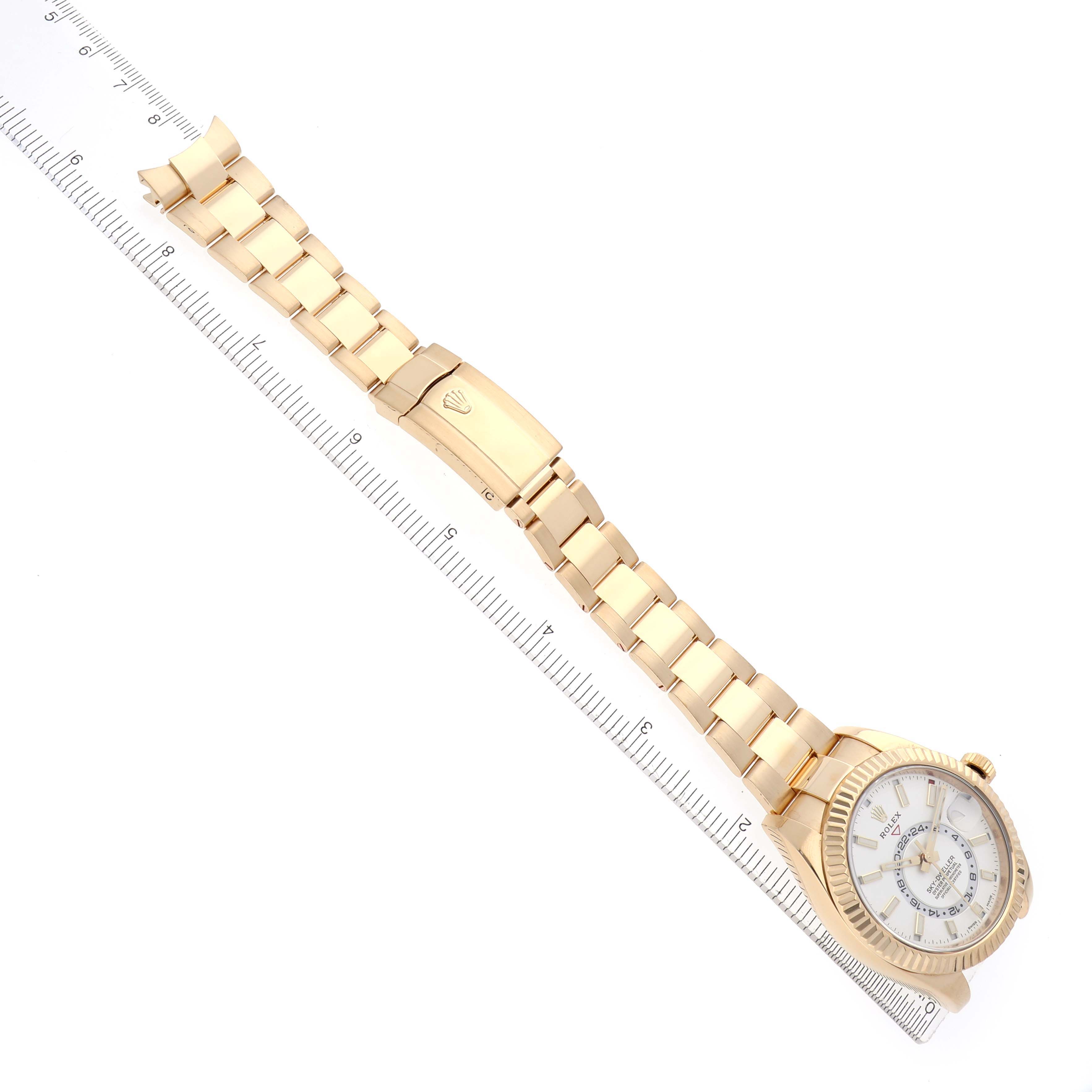The Rolex Sky-Dweller 326938 Men
s Yellow Gold White Dial 326938 Men
s Yellow Gold White Dial watch is shown at an angled top view, displaying the full bracelet and clasp alongside a ruler for scale.