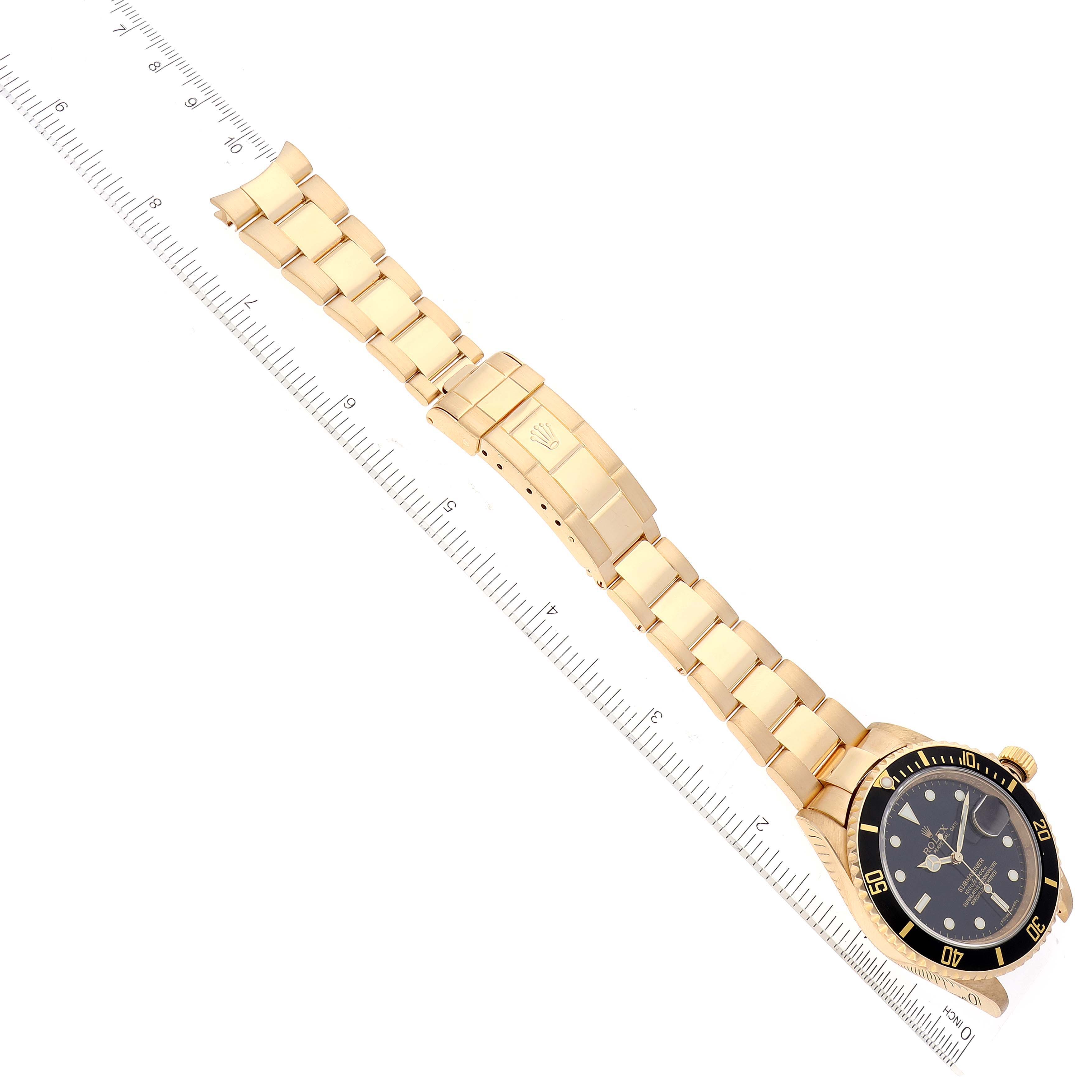 The Rolex Submariner 16618 Men's Yellow Gold Black Dial 16618 Men's Yellow Gold Black Dial watch is shown from a top-down angle, displaying the full watch, including the strap and clasp alongside a ruler for scale.