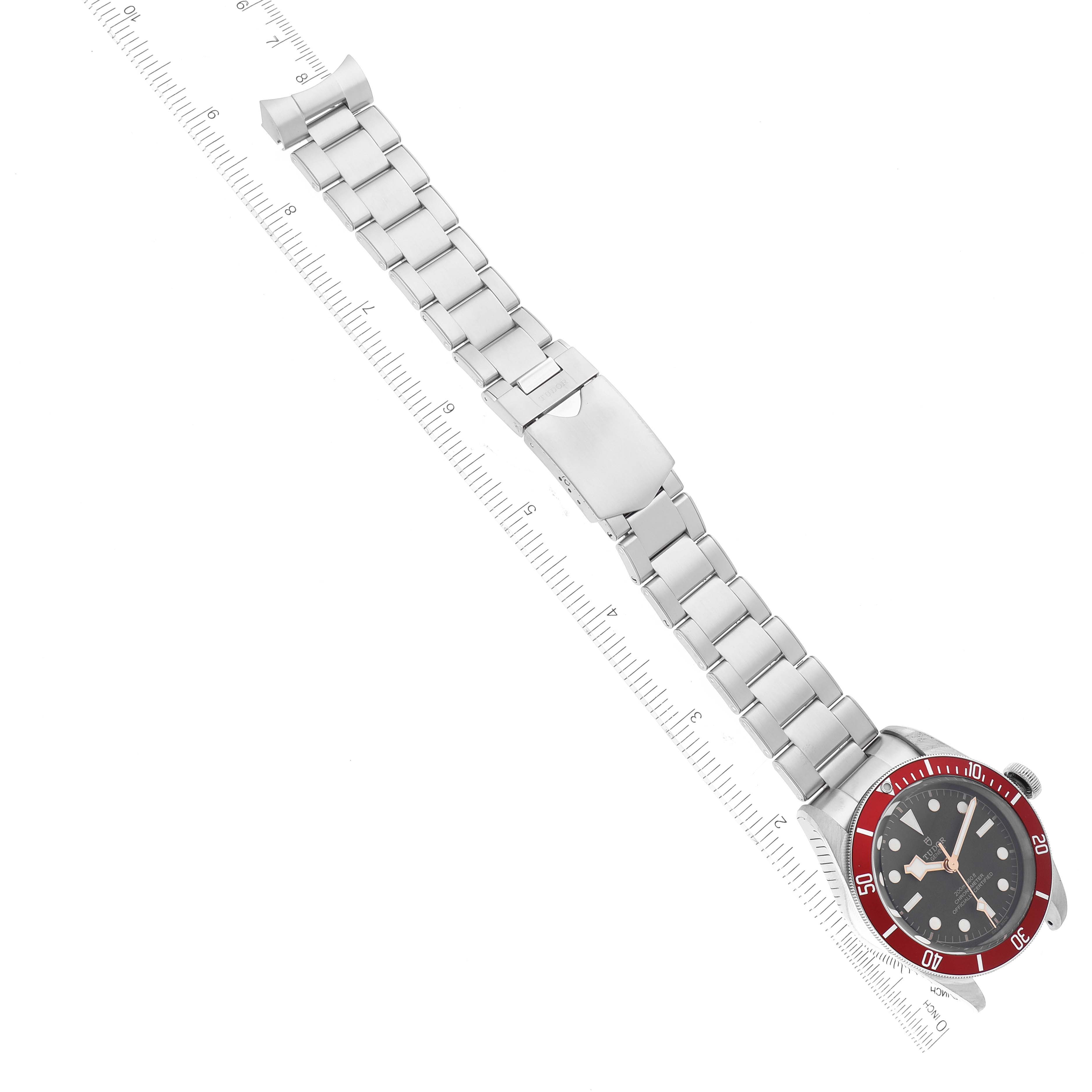 The Tudor Heritage Black Bay 79230R Men
s Stainless Steel Black Dial 79230R Men
s Stainless Steel Black Dial watch is shown from an overhead angle, featuring its face and metal bracelet with a ruler for size reference.