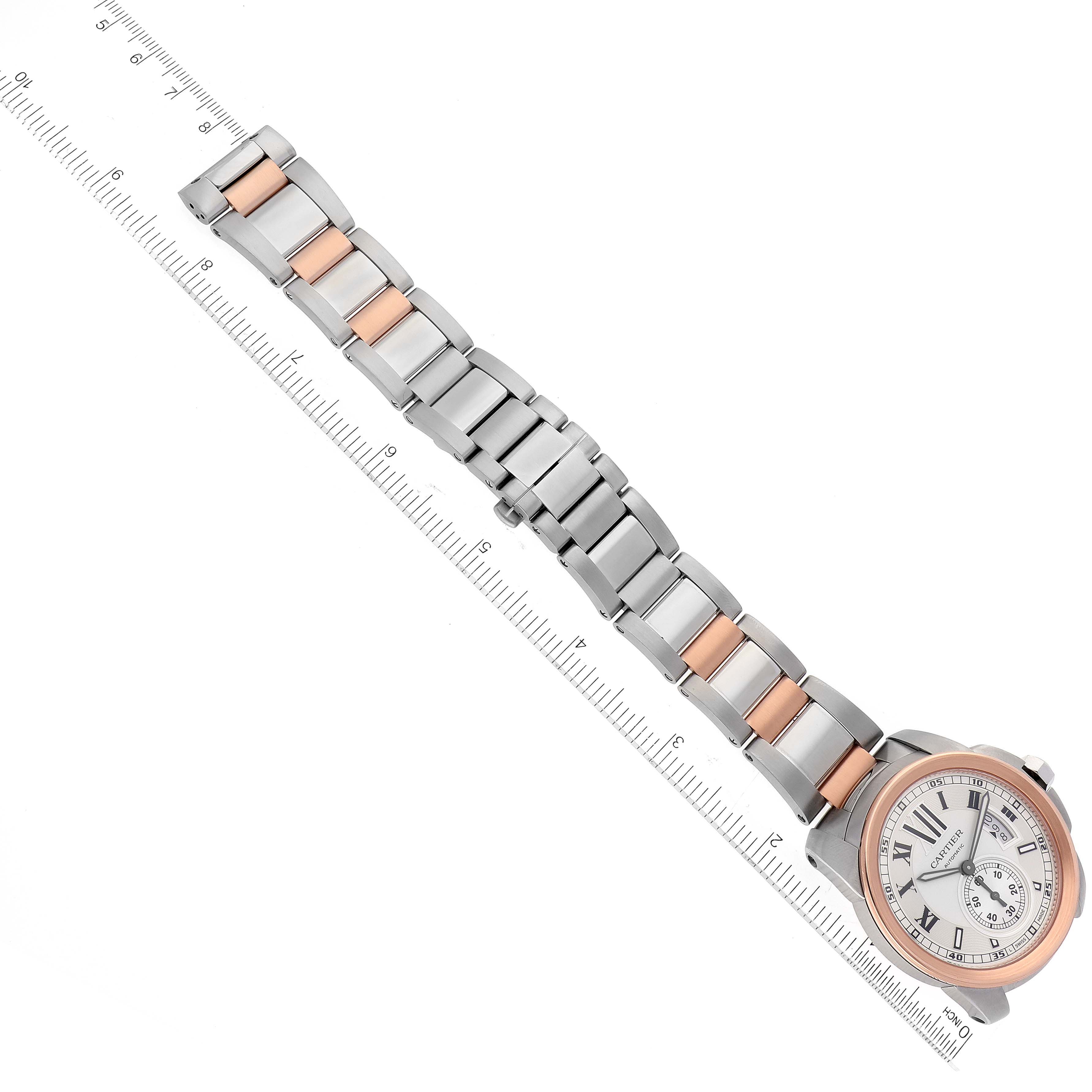 The image shows a top-down view of the Calibre de Cartier watch by Cartier, highlighting its face and two-tone metal bracelet with a ruler for scale.