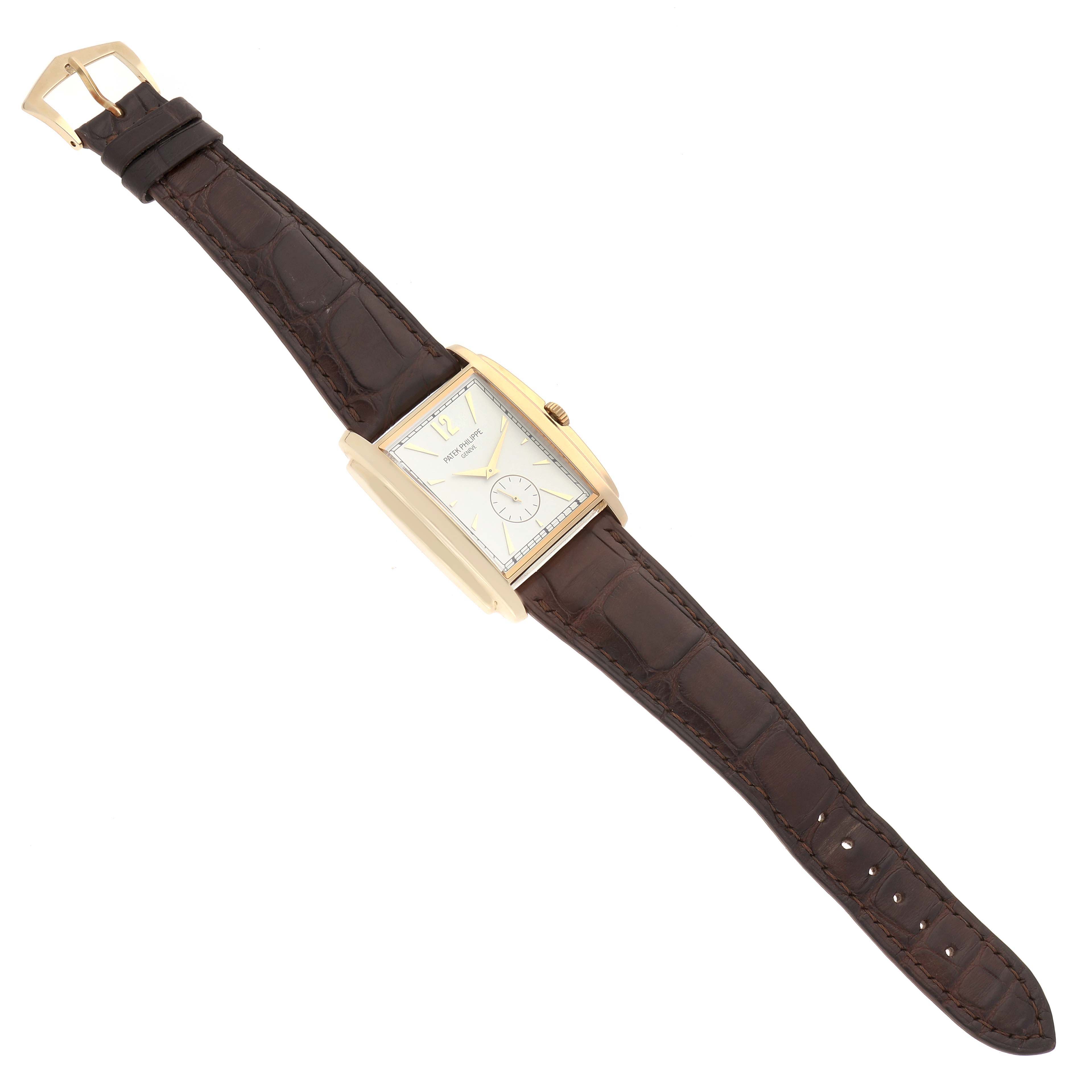 The Patek Philippe Gondolo 5124J-001 Men
s Yellow Gold Silver Dial 5124J-001 Men
s Yellow Gold Silver Dial watch is shown from a top-down angle, displaying its rectangular face, brown leather strap, and gold buckle.