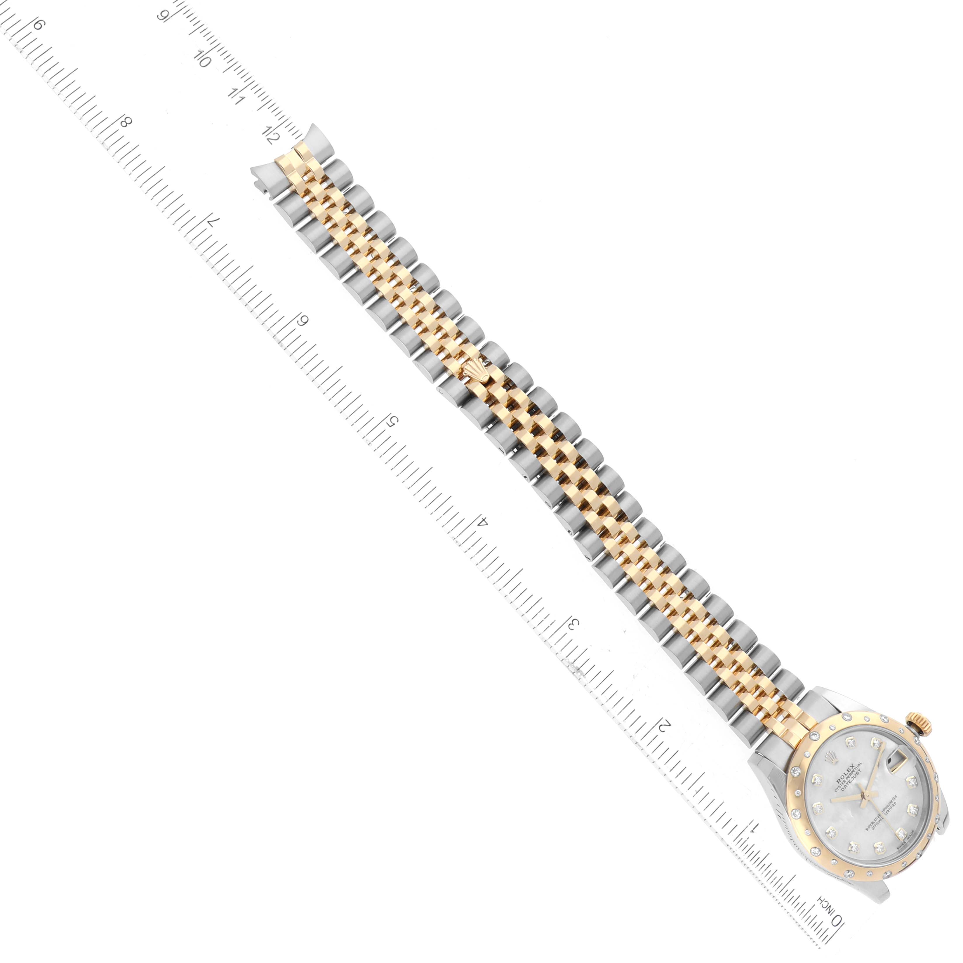 The image shows a Rolex Mid-Size 178343 Women's Steel and Gold (two tone) Mother of Pearl Dial 178343 Women's Steel and Gold (two tone) Mother of Pearl Dial model watch with a two-tone metal bracelet and face, viewed from an aerial angle beside a ruler.