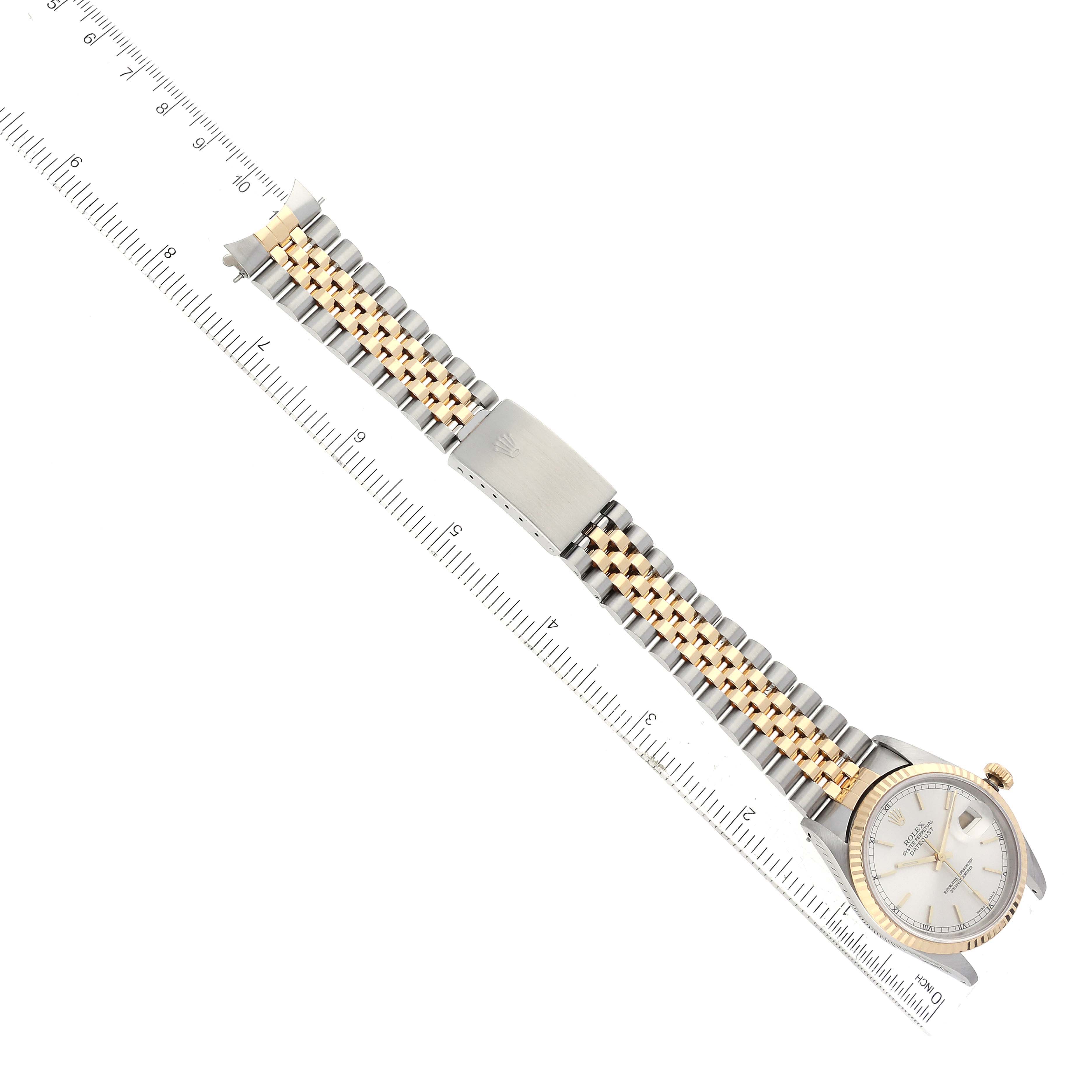 The image shows a top-down view of a Rolex Datejust 16233 Men's Steel and Gold (two tone) Silver Dial 16233 Men's Steel and Gold (two tone) Silver Dial watch, displaying the face and bracelet alongside a ruler for scale.