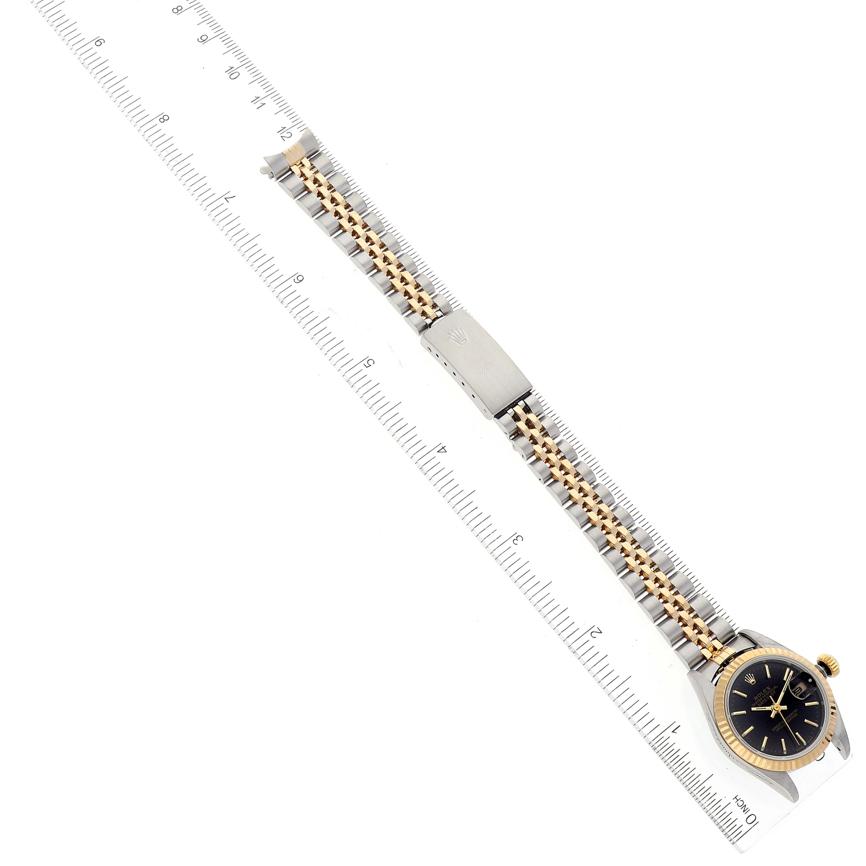The image shows the Rolex Datejust 79173 Women's Steel and Gold (two tone) Black Dial 79173 Women's Steel and Gold (two tone) Black Dial watch laid flat next to a ruler, displaying the entire band and watch face.