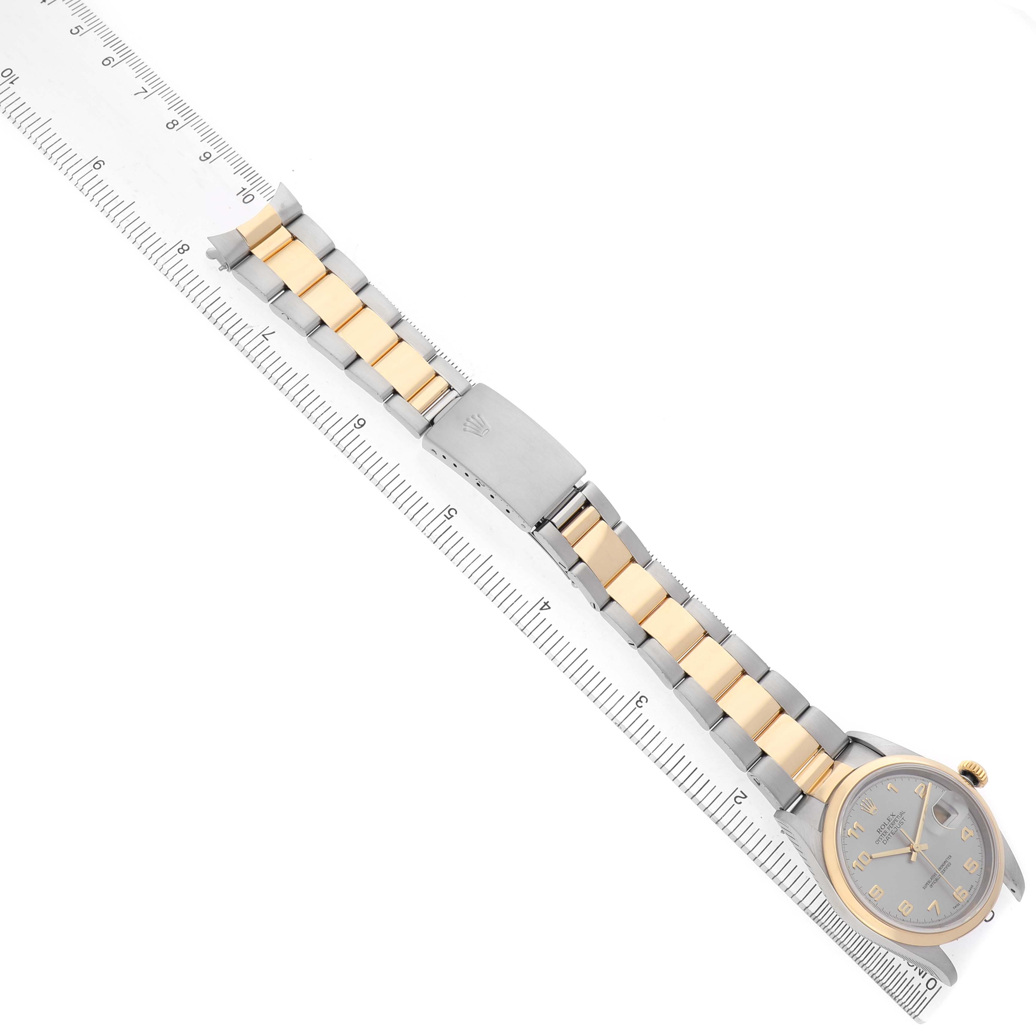 The Rolex Datejust 16203 Men's Steel and Gold (two tone) Silver Dial watch is shown from an overhead angle, displaying its face and two-tone bracelet alongside a ruler.