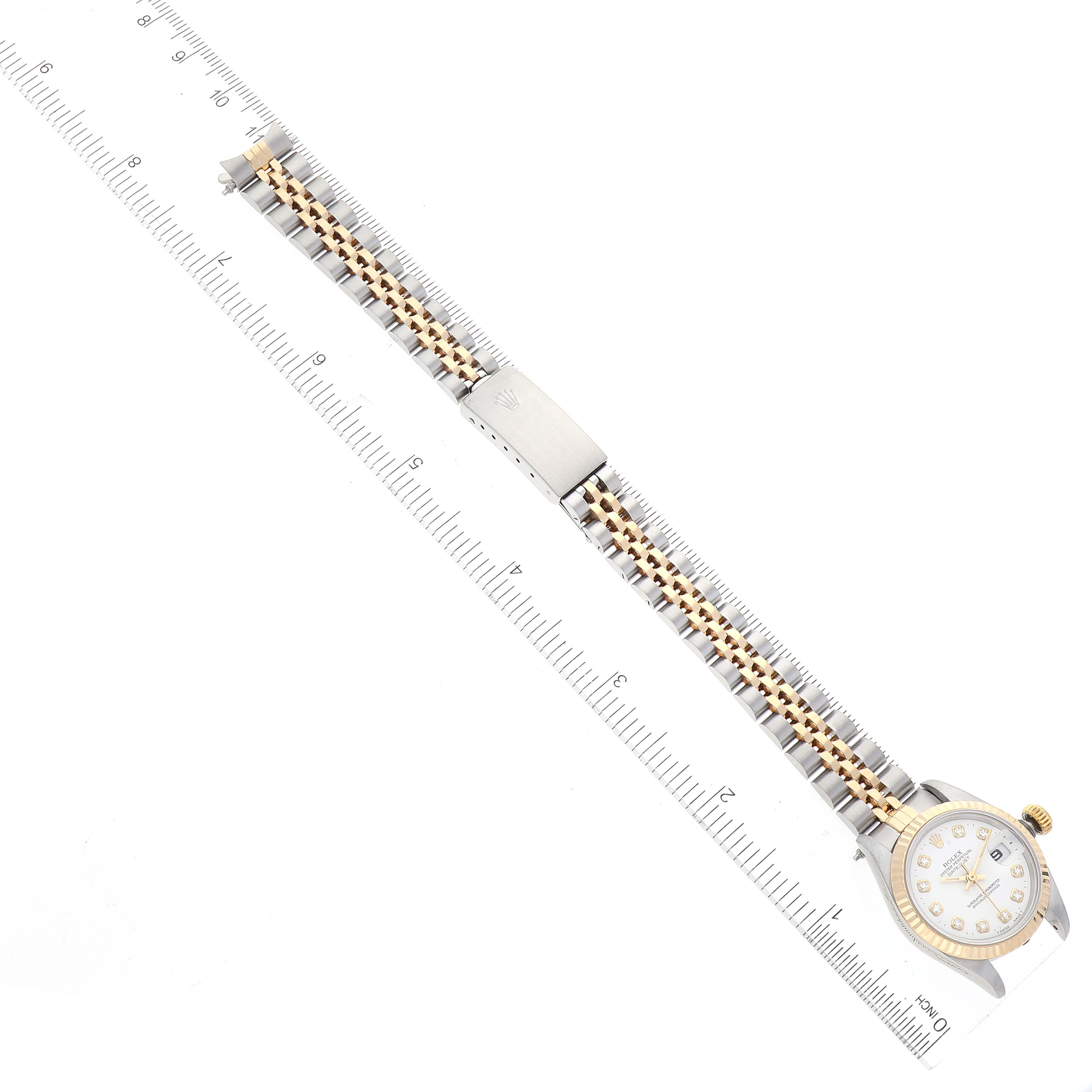 This image shows a Rolex Datejust 69173 Women
s Steel and Gold (two tone) White Dial 69173 Women
s Steel and Gold (two tone) White Dial watch from a top-down angle, displaying its face, bracelet, and clasp along a ruler for scale.