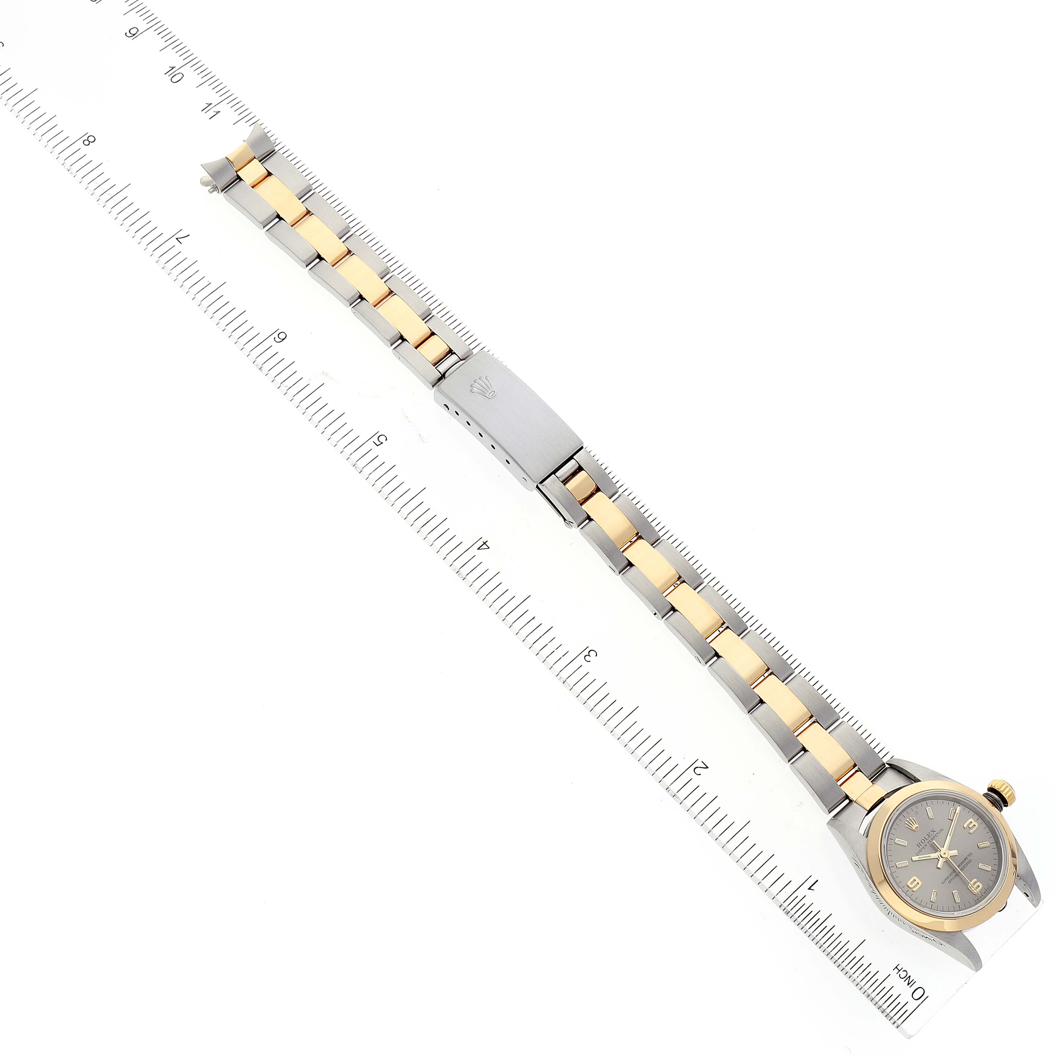 The image shows a Rolex Oyster Perpetual 76183 Women
s Steel and Gold (two tone) Grey Dial 76183 Women
s Steel and Gold (two tone) Grey Dial watch and its bracelet laid flat next to a ruler, highlighting its length and design.
