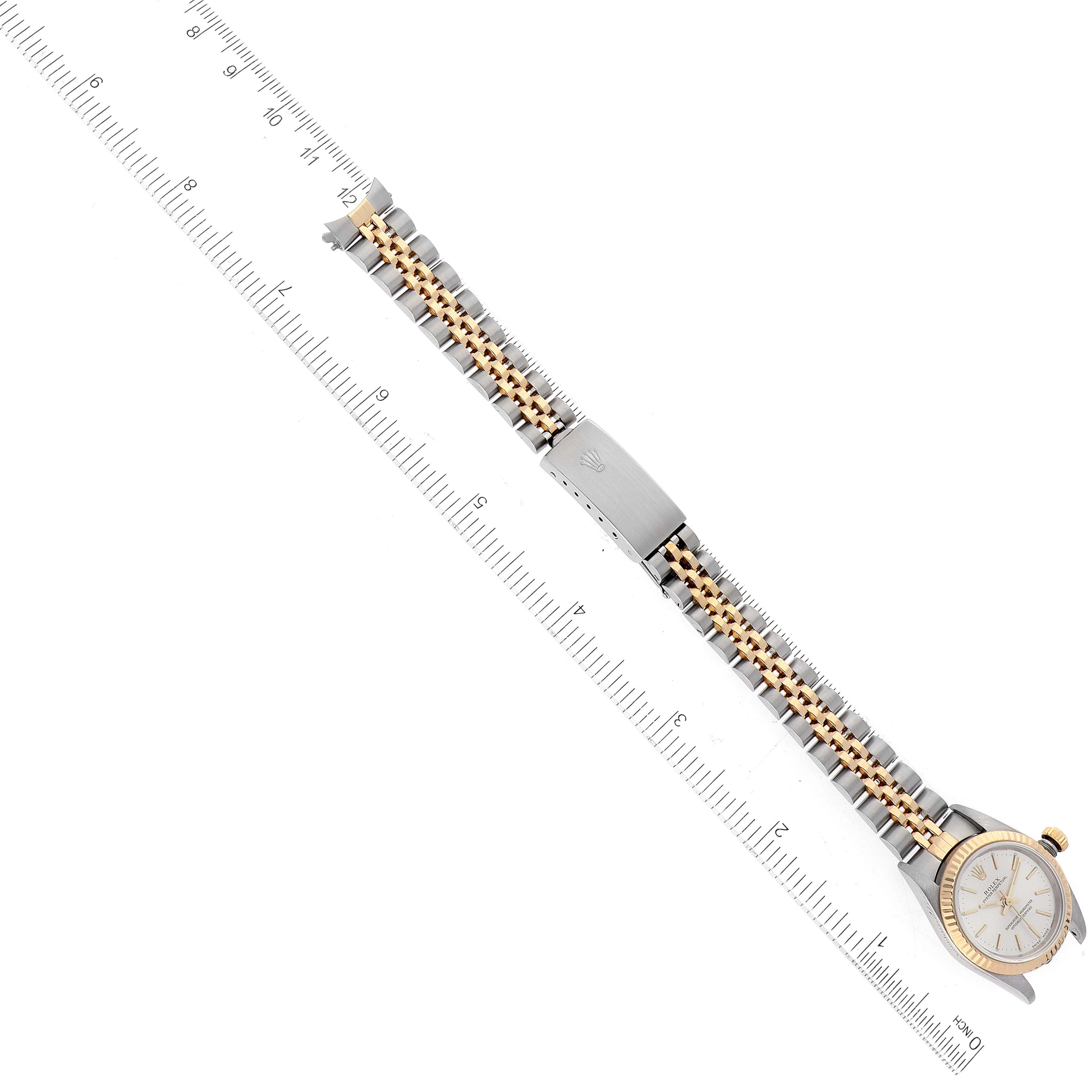 The image shows an overhead view of a Rolex Oyster Perpetual 76193 Women's Steel and Gold (two tone) Silver Dial 76193 Women's Steel and Gold (two tone) Silver Dial watch and its two-tone bracelet against a measuring ruler.
