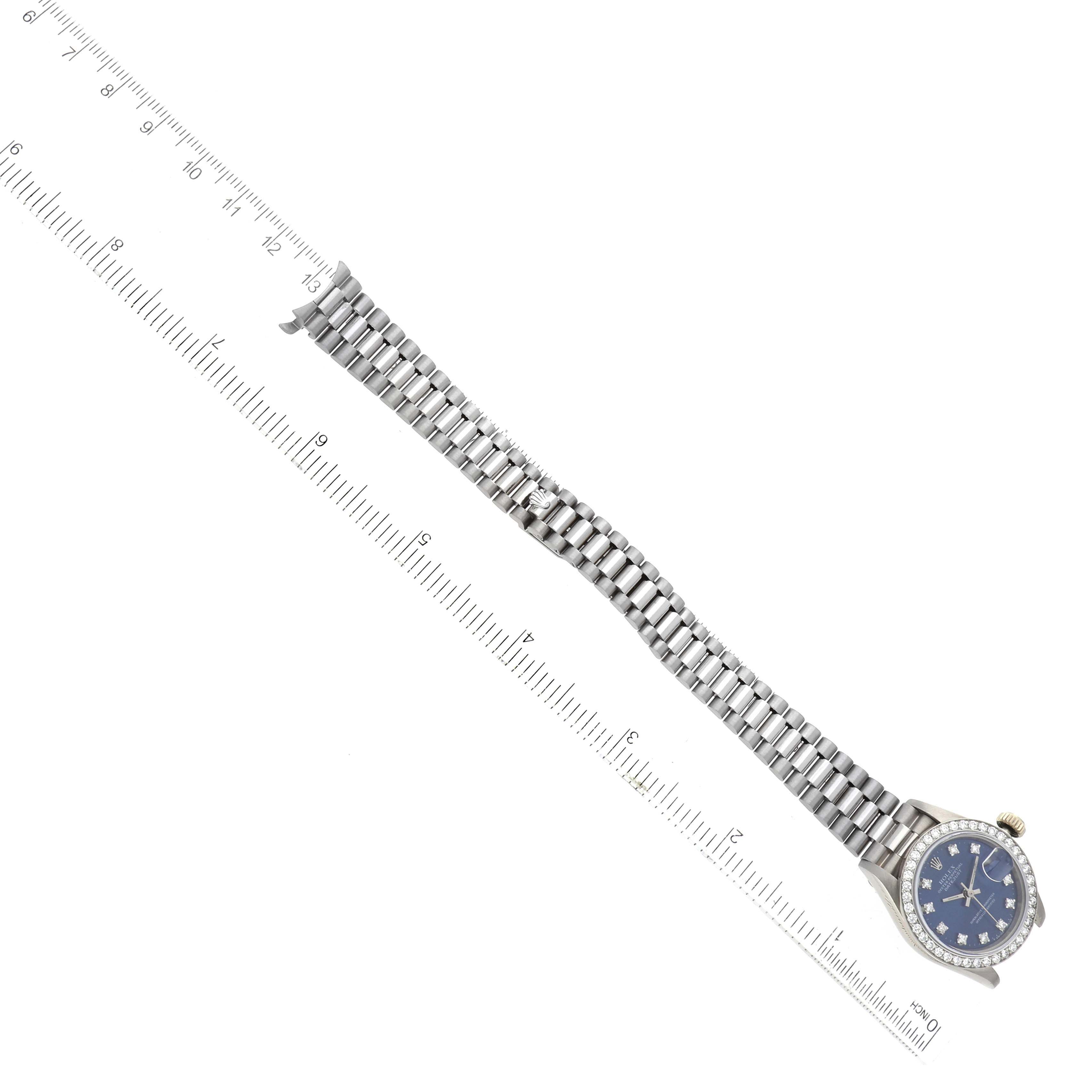 The image shows a Rolex President 69139 Women's White Gold Blue Dial 69139 Women's White Gold Blue Dial model watch laid flat alongside a ruler, highlighting its band and blue face with diamond markers.