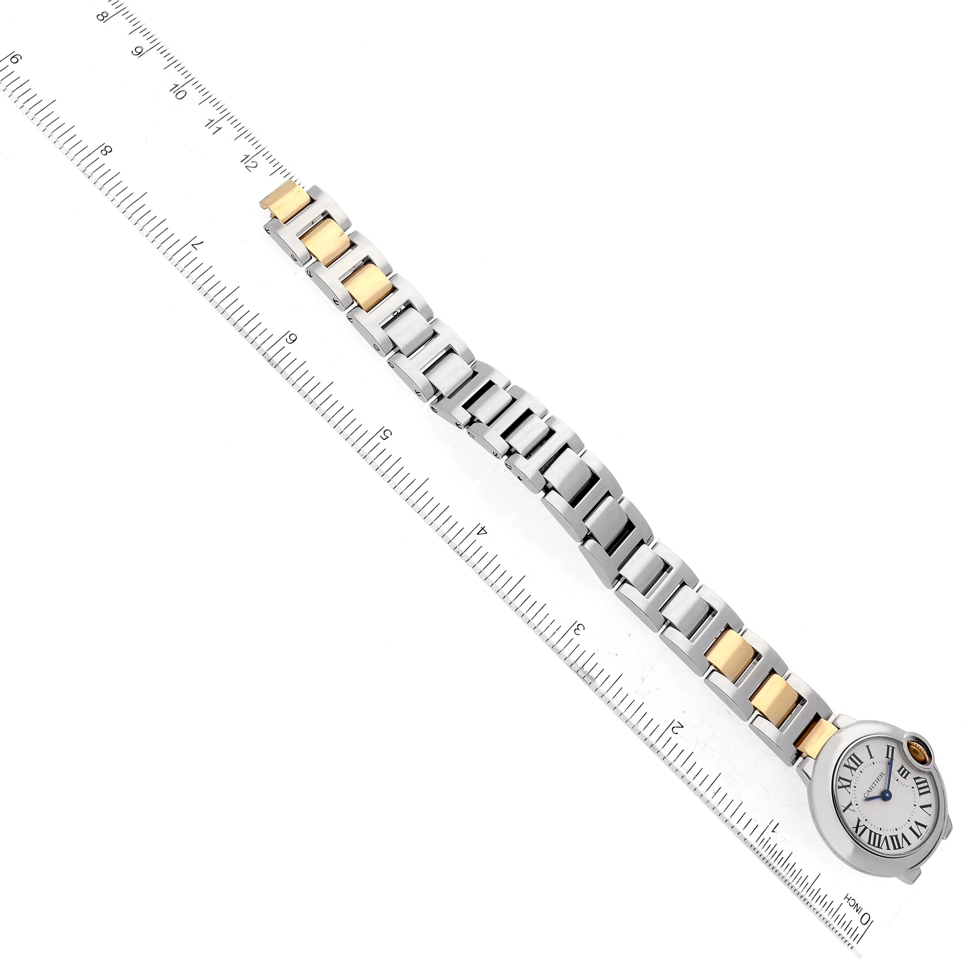 The image shows a top-down view of the Ballon Bleu model by Cartier, focusing on its gold and silver bracelet beside a ruler for scale.