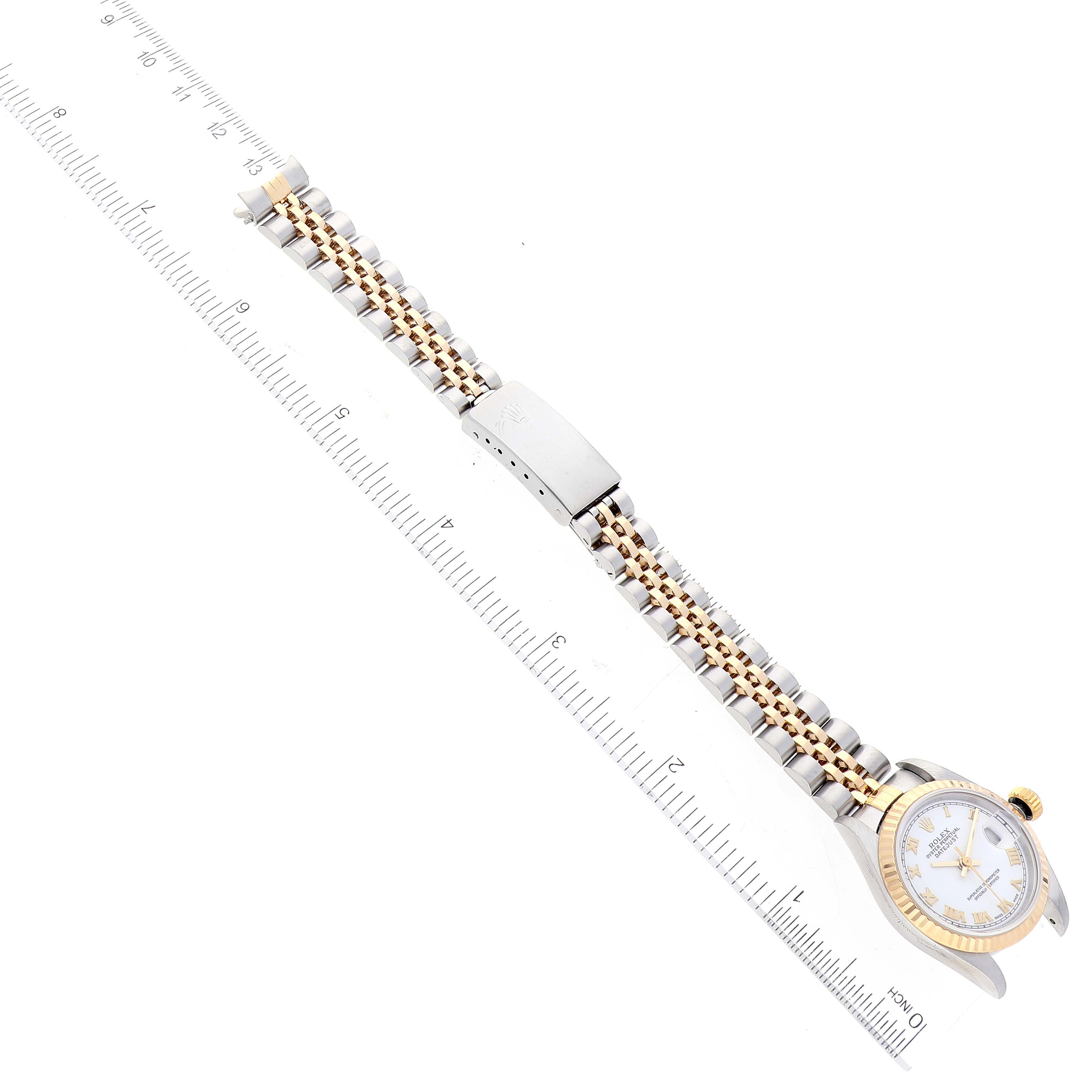 The image shows a Rolex Datejust 79173 Women's Steel and Gold (two tone) White Dial 79173 Women's Steel and Gold (two tone) White Dial watch positioned flat on its side, displaying the face, band, and clasp with a ruler for scale.