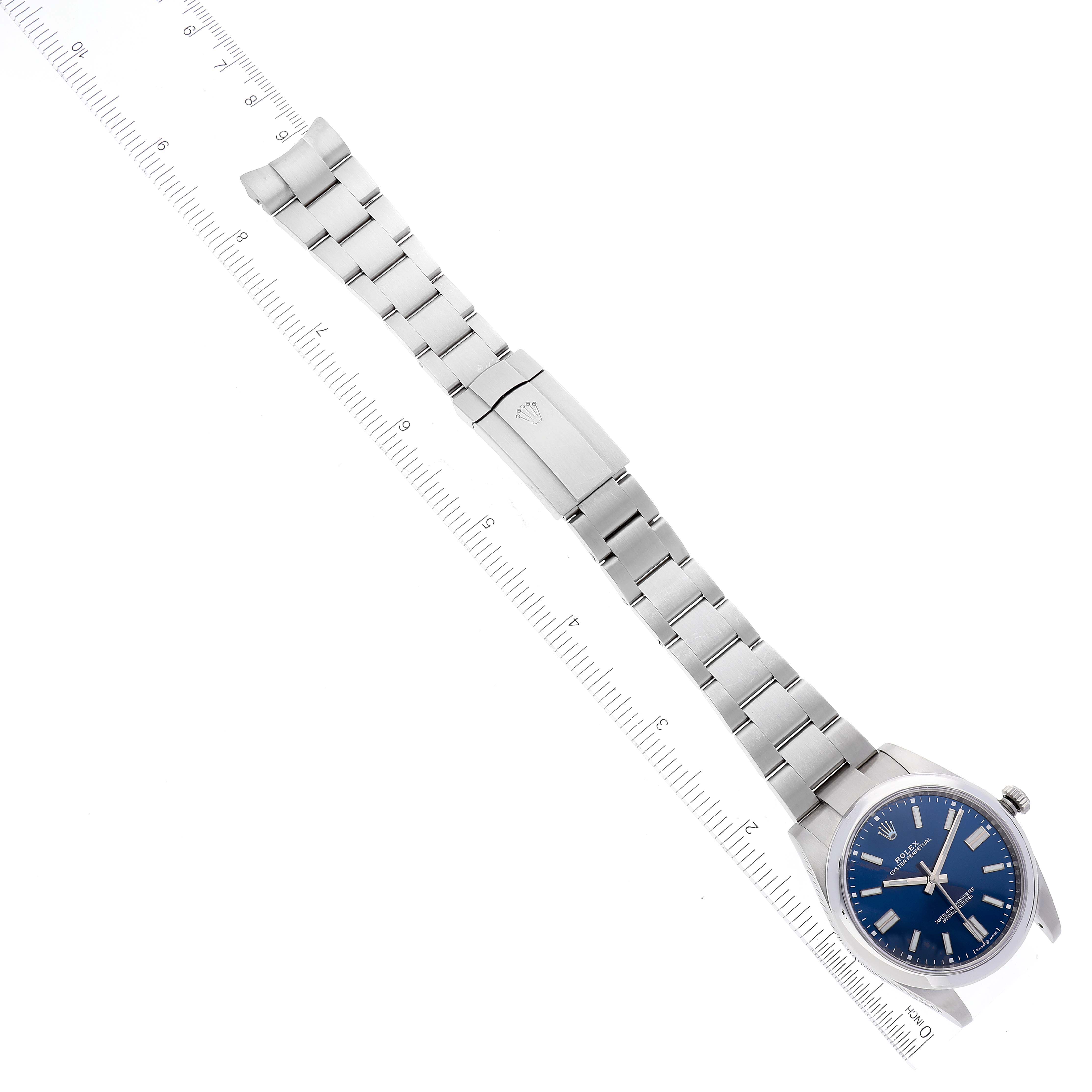 The image shows a full top-down view of the Rolex Oyster Perpetual 124300 Men's Stainless Steel Blue Dial 124300 Men's Stainless Steel Blue Dial watch, including the dial, bezel, case, bracelet, and clasp alongside a ruler for measurement.