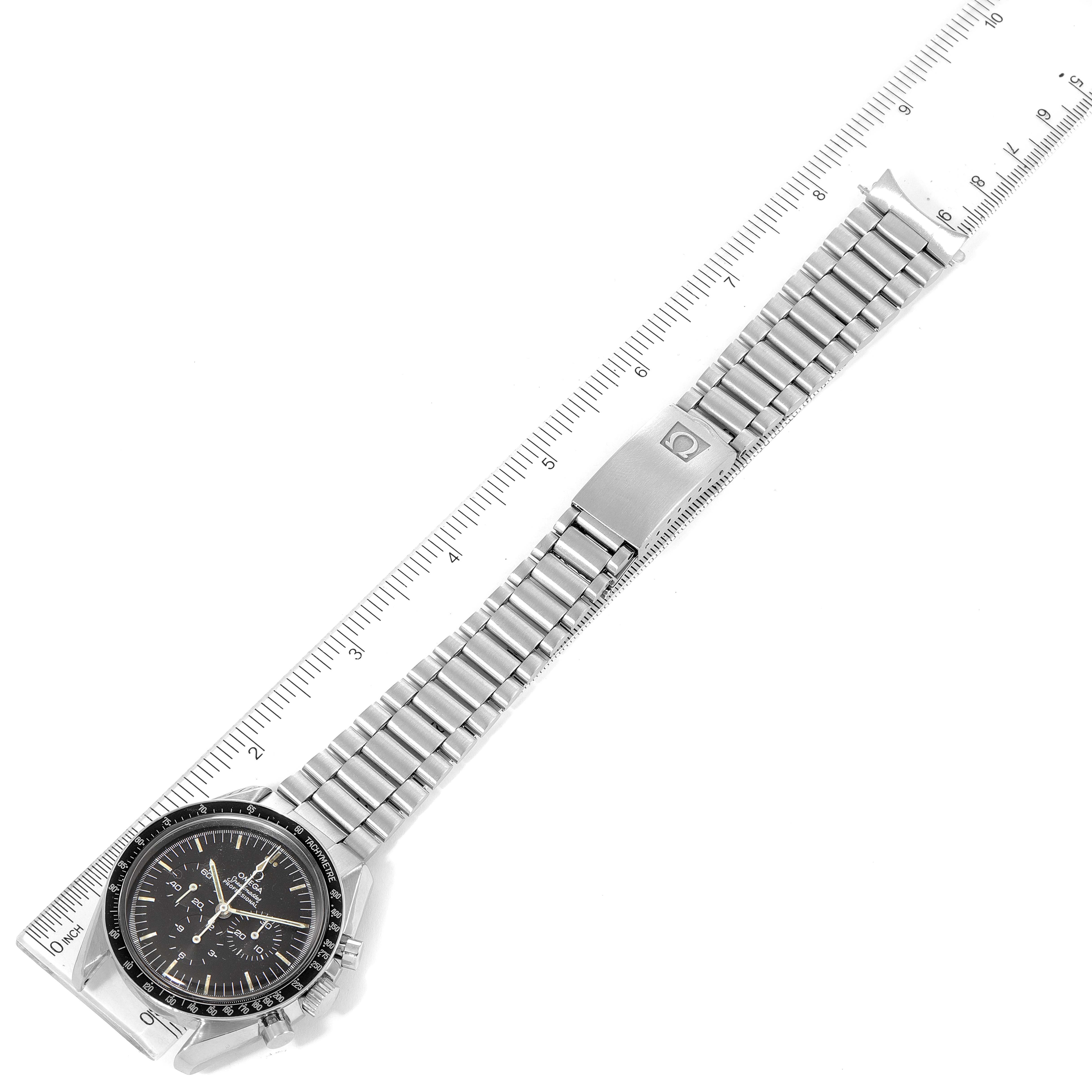 The image shows a top view of an Omega Speedmaster 145.022 Men's Stainless Steel Black Dial 145.022 Men's Stainless Steel Black Dial watch with its metal bracelet fully extended and aligned next to a ruler for scale.