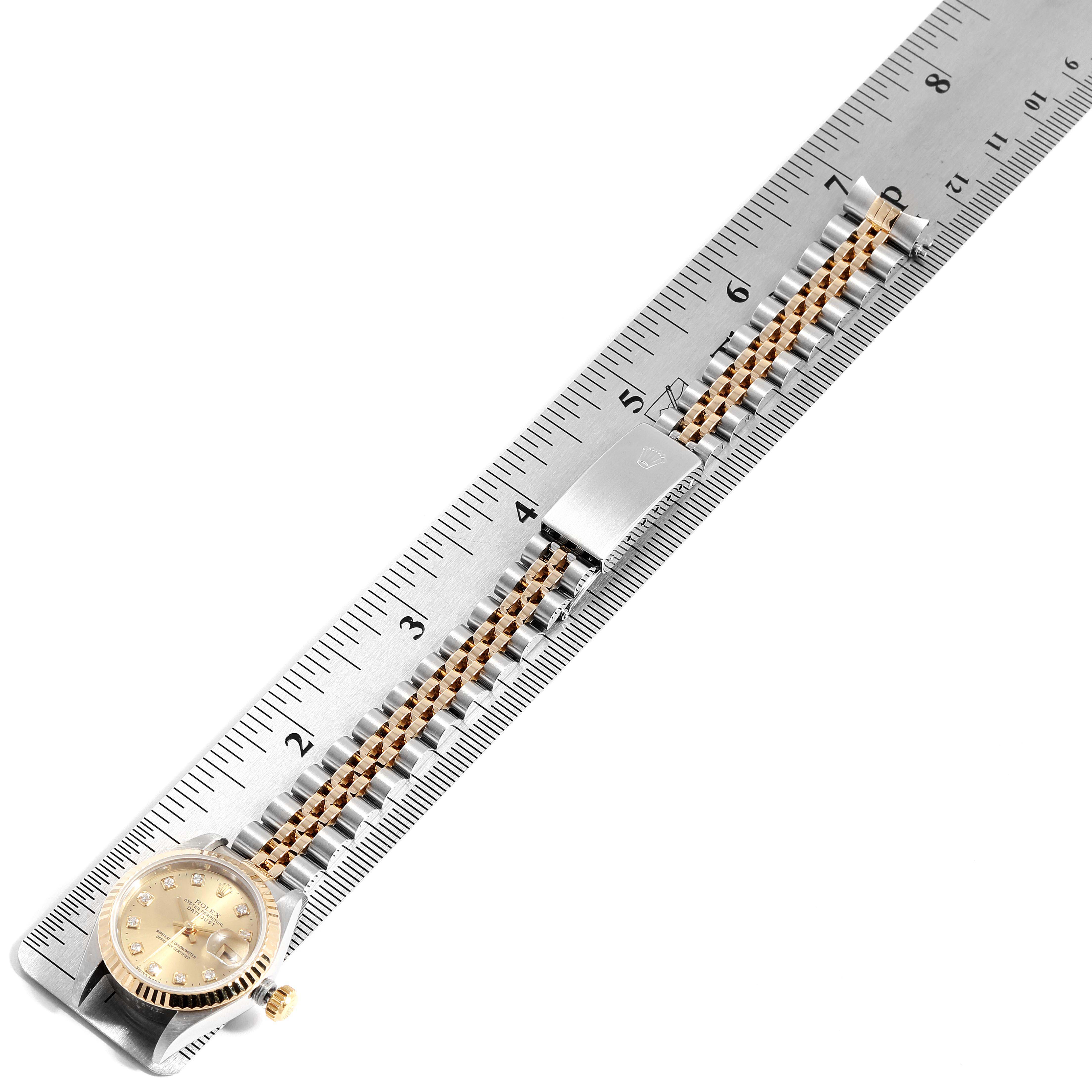 This image shows a Rolex Datejust 69173 Women
s Steel and Gold (two tone) Champagne Dial 69173 Women
s Steel and Gold (two tone) Champagne Dial watch laid out on a ruler, showing the watch face and the bracelet with clasp.