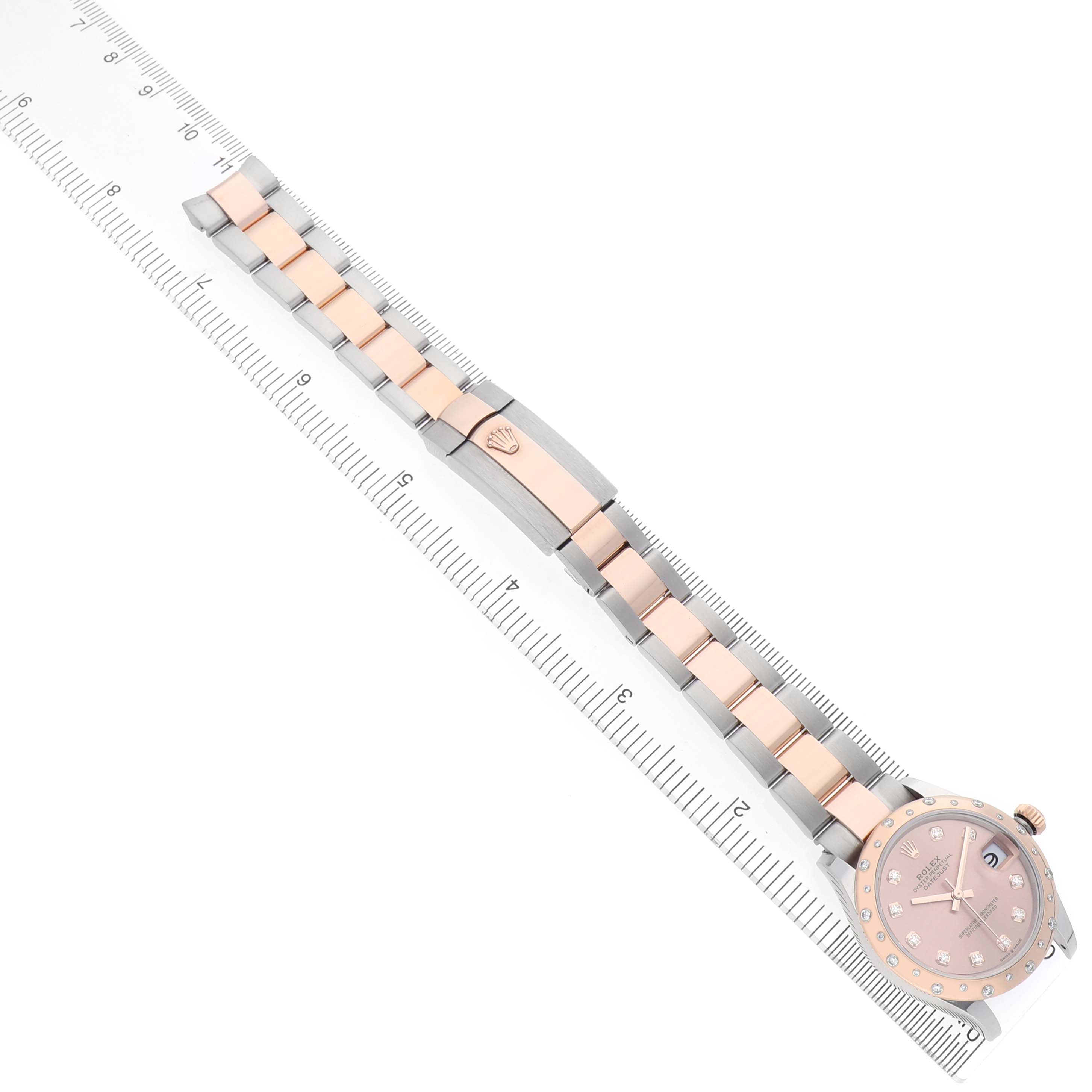 The Rolex Mid-Size 278341RBR Women's Stainless Steel Pink Dial watch is shown from an overhead angle, highlighting the bracelet, clasp, and face alongside a ruler for scale.