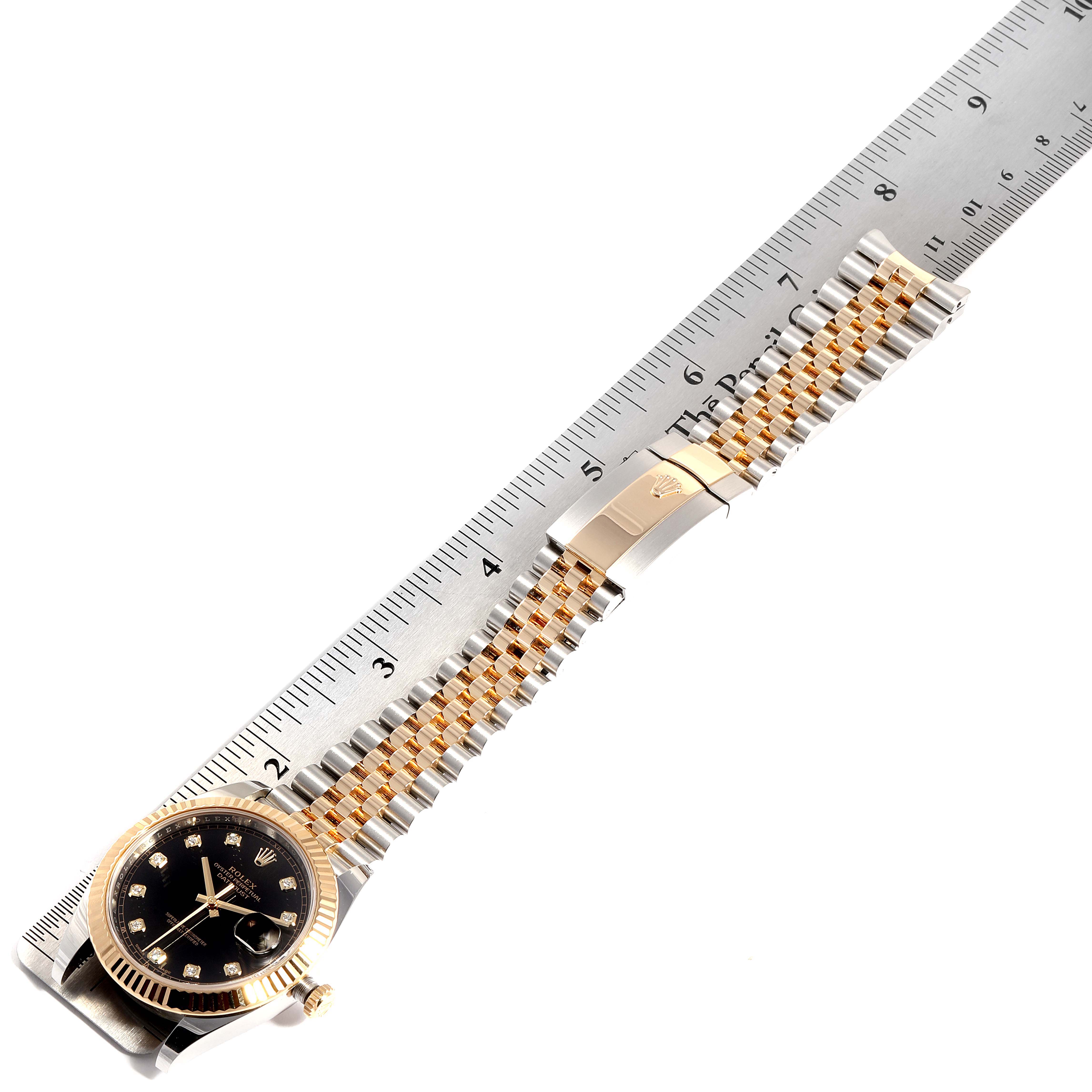 The image shows a Rolex Datejust 126333 Men's Steel and Gold (two tone) Black Dial 126333 Men's Steel and Gold (two tone) Black Dial watch laid flat beside a ruler, displaying its black dial, bezel, and Jubilee bracelet in full view.