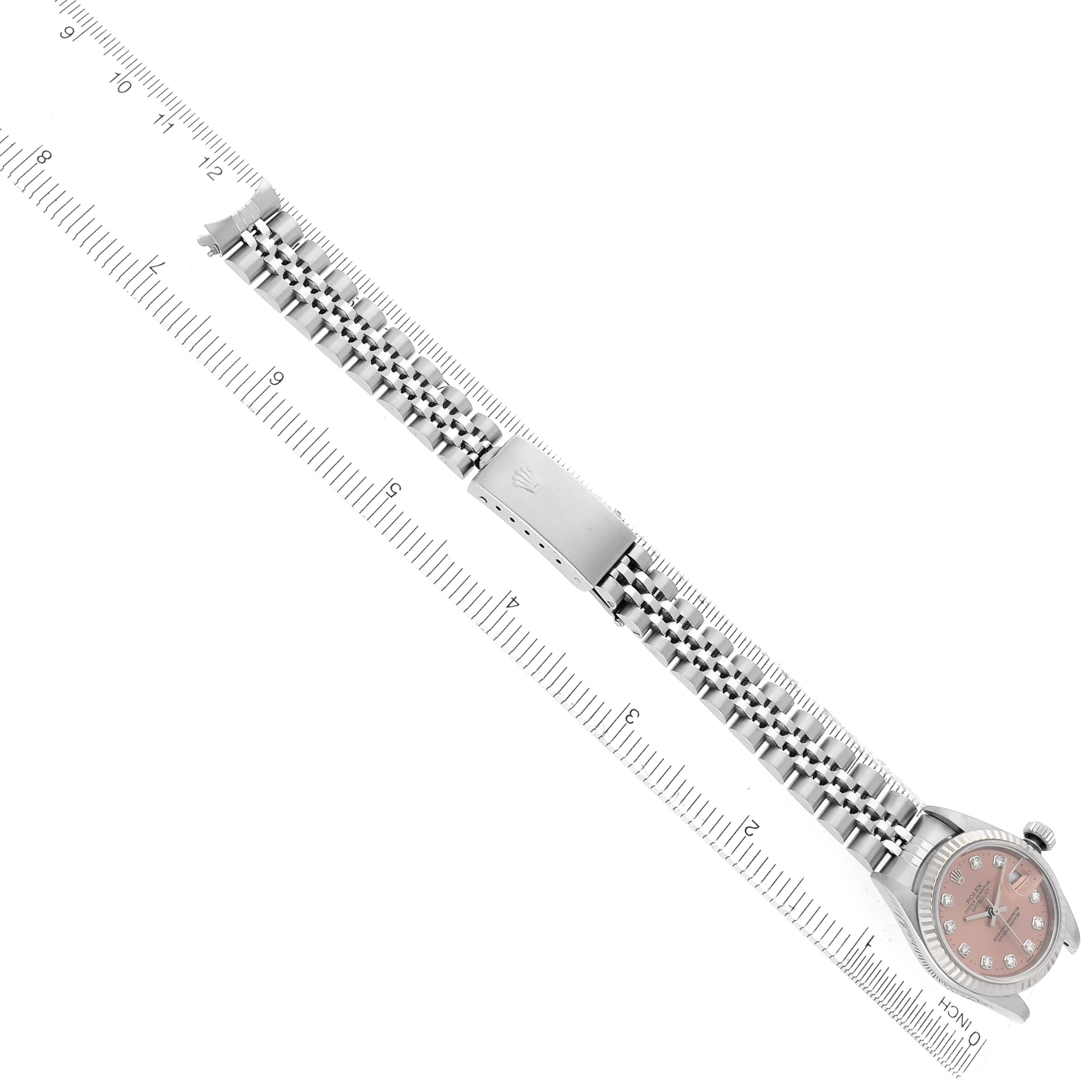 The image shows a Rolex Datejust 79174 Women
s Stainless Steel Pink Dial 79174 Women
s Stainless Steel Pink Dial watch laid flat with a pink dial, bracelet, and clasp visible, next to a ruler for scale.