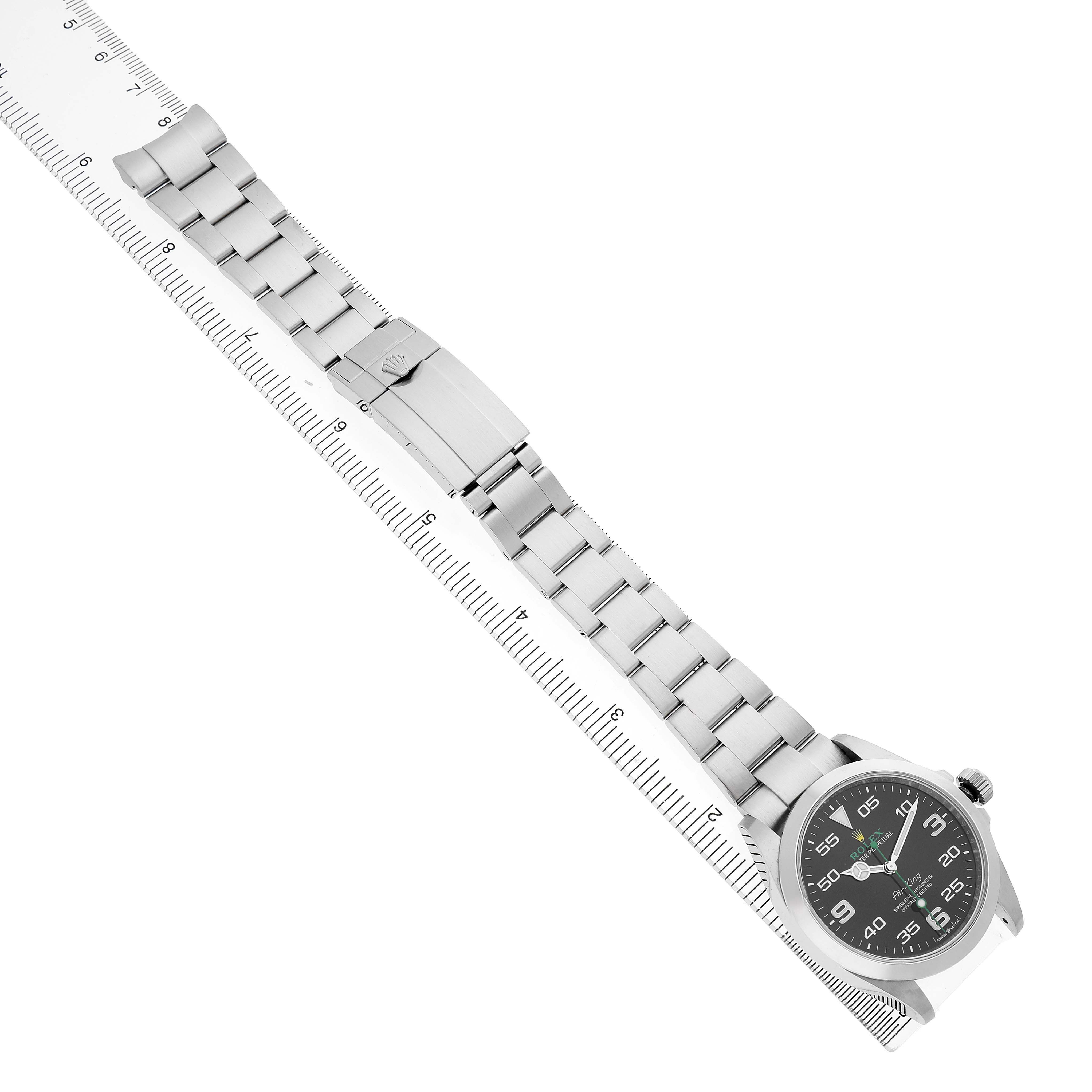 The Rolex Air-King 126900 Men's Stainless Steel Black Dial watch is shown from a top view, displaying the dial, bracelet, and clasp, placed alongside a ruler for scale.