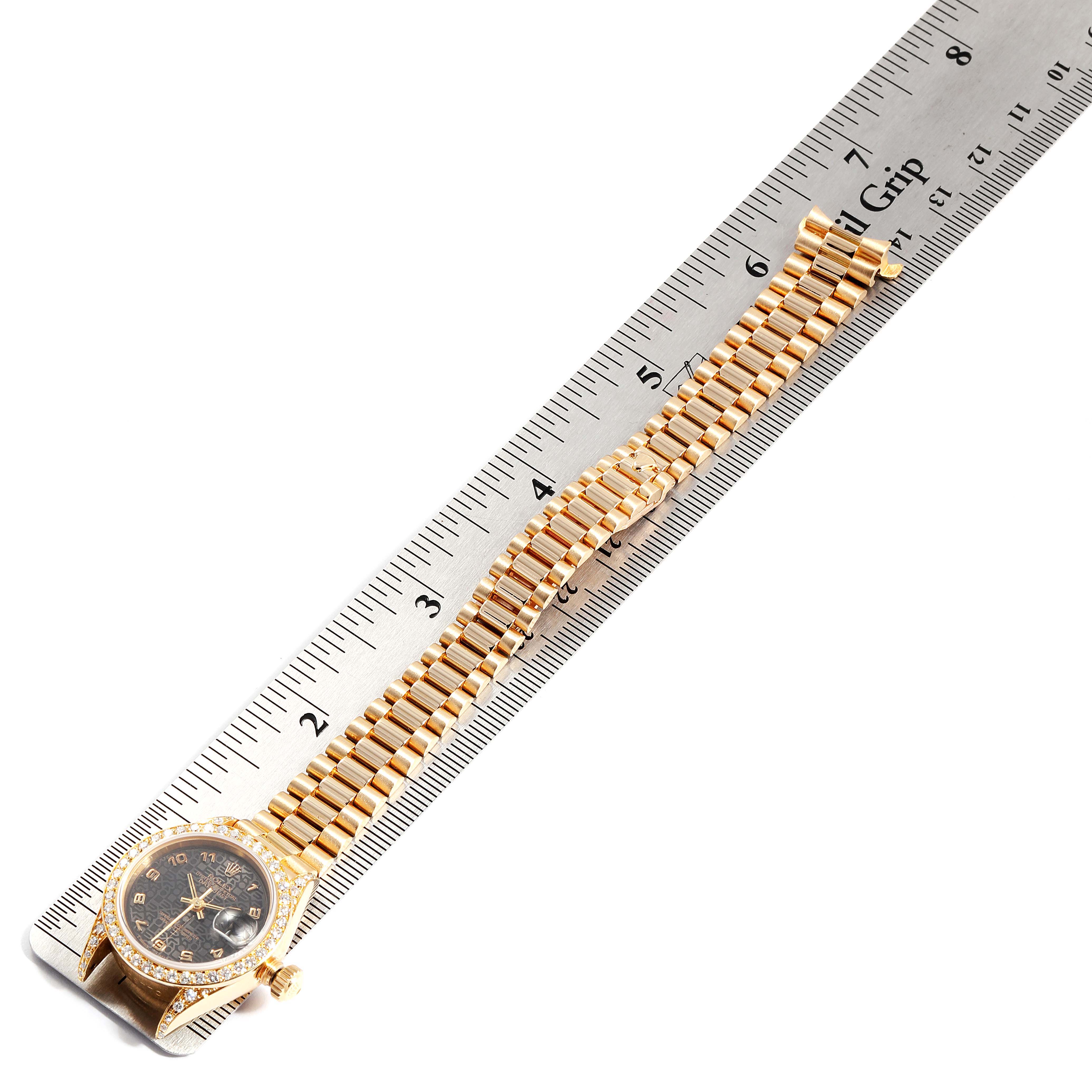 The image shows a Rolex President 69038 Women's Yellow Gold Black Dial 69038 Women's Yellow Gold Black Dial model watch laid flat alongside a ruler, showcasing its entire bracelet and watch face.