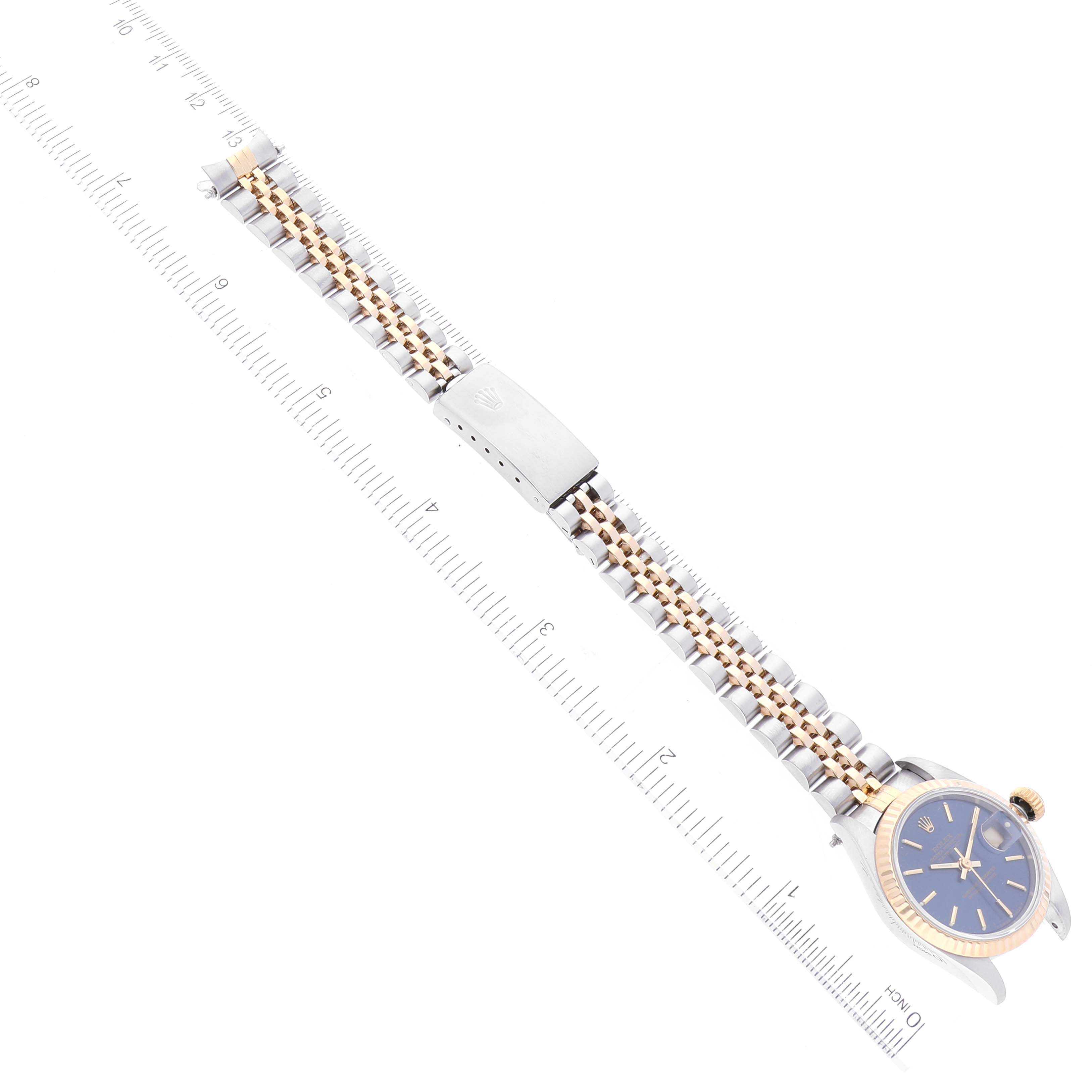 The Rolex Datejust 69173 Women's Steel and Gold (two tone) Blue Dial 69173 Women's Steel and Gold (two tone) Blue Dial watch is shown from an aerial view displaying its face, bracelet, and clasp alongside a ruler for scale.