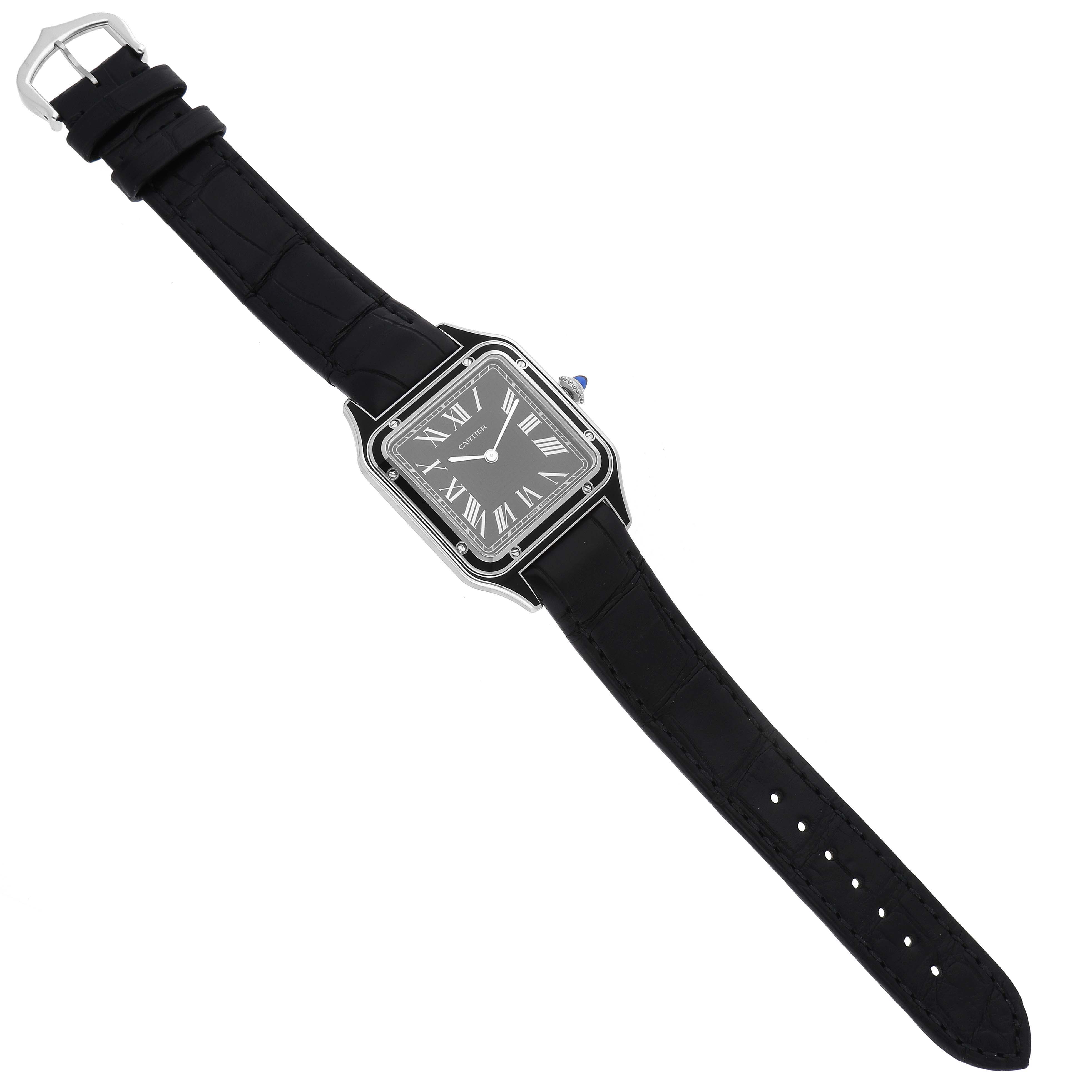 The image shows a Cartier Santos Dumont WSSA0046 Men's Stainless Steel Black Dial WSSA0046 Men's Stainless Steel Black Dial watch in a top-down view, displaying its black strap, square face, and Roman numeral dial.