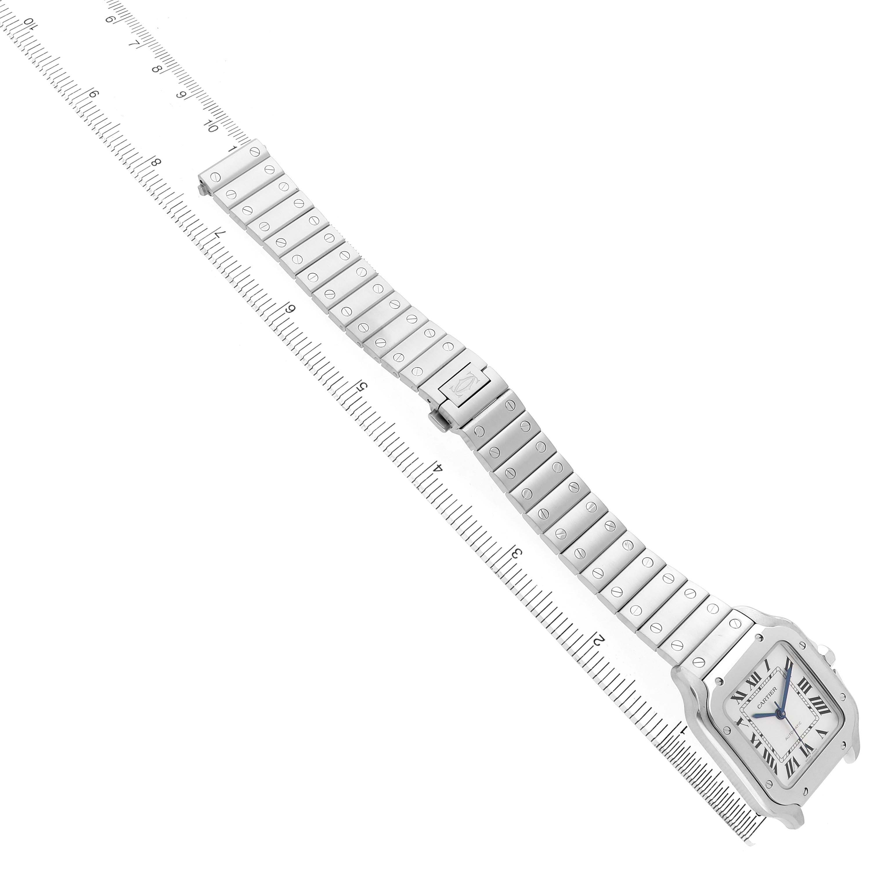 The image shows a Cartier Santos WSSA0029 Men's Stainless Steel Silver Dial watch at a diagonal angle, highlighting the face and full metal bracelet, with a ruler alongside.