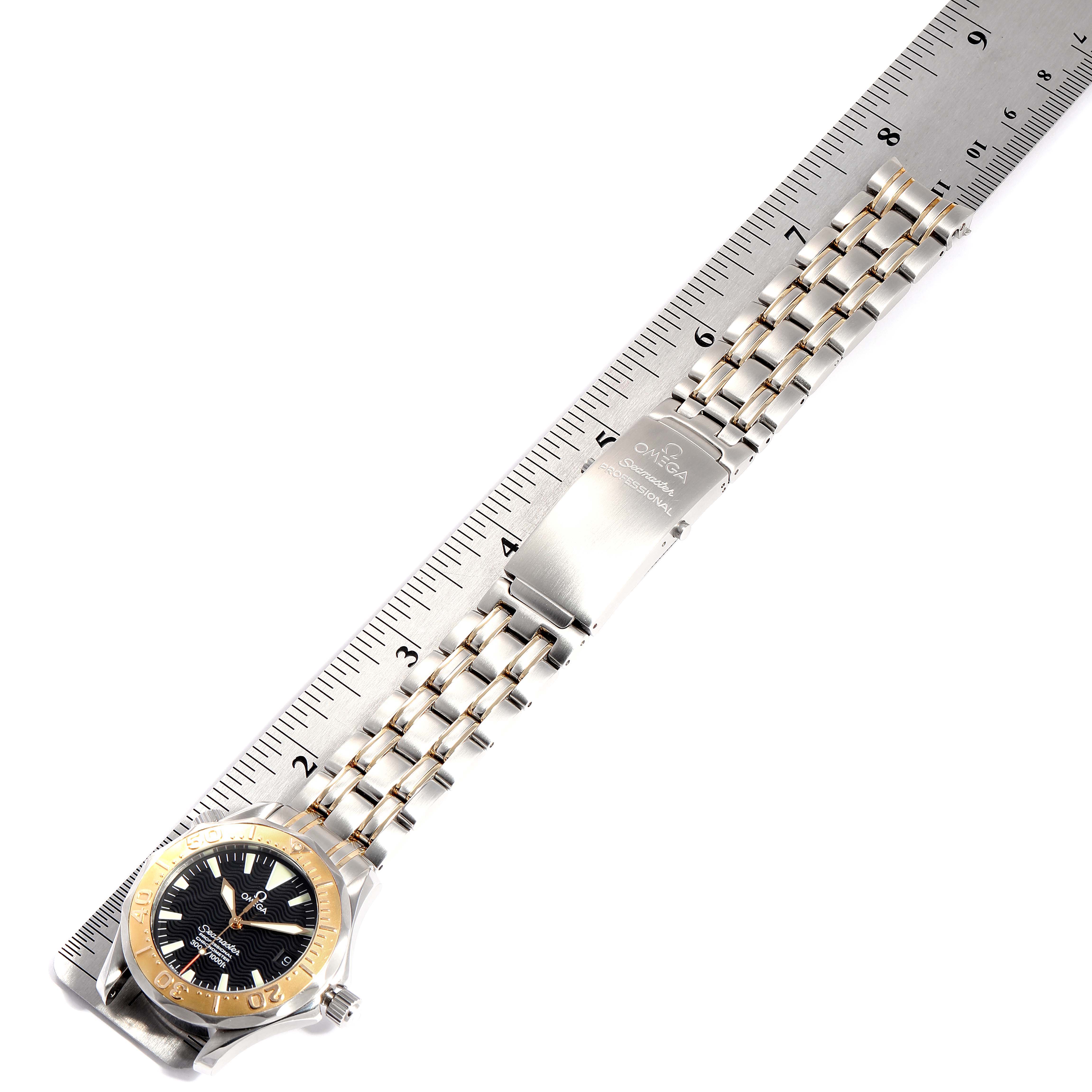 The image shows the Omega Seamaster 2453.50.00 Men's Steel and Gold (two tone) Black Dial 2453.50.00 Men's Steel and Gold (two tone) Black Dial watch laying flat with its stainless steel bracelet fully extended alongside a ruler.