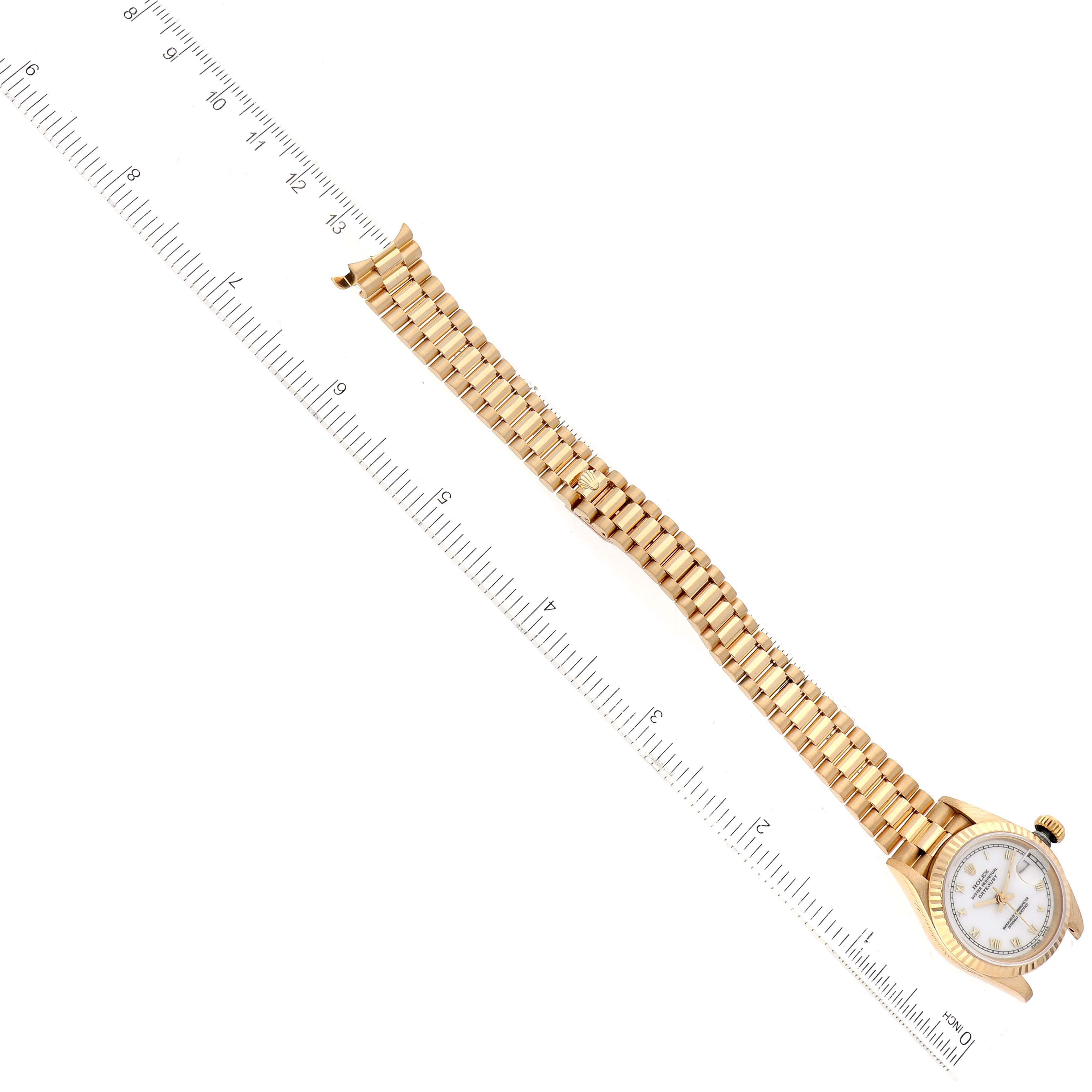 The image shows a Rolex President 69178 Women's Yellow Gold White Dial 69178 Women's Yellow Gold White Dial model watch placed diagonally next to a ruler, displaying its entire band and face.