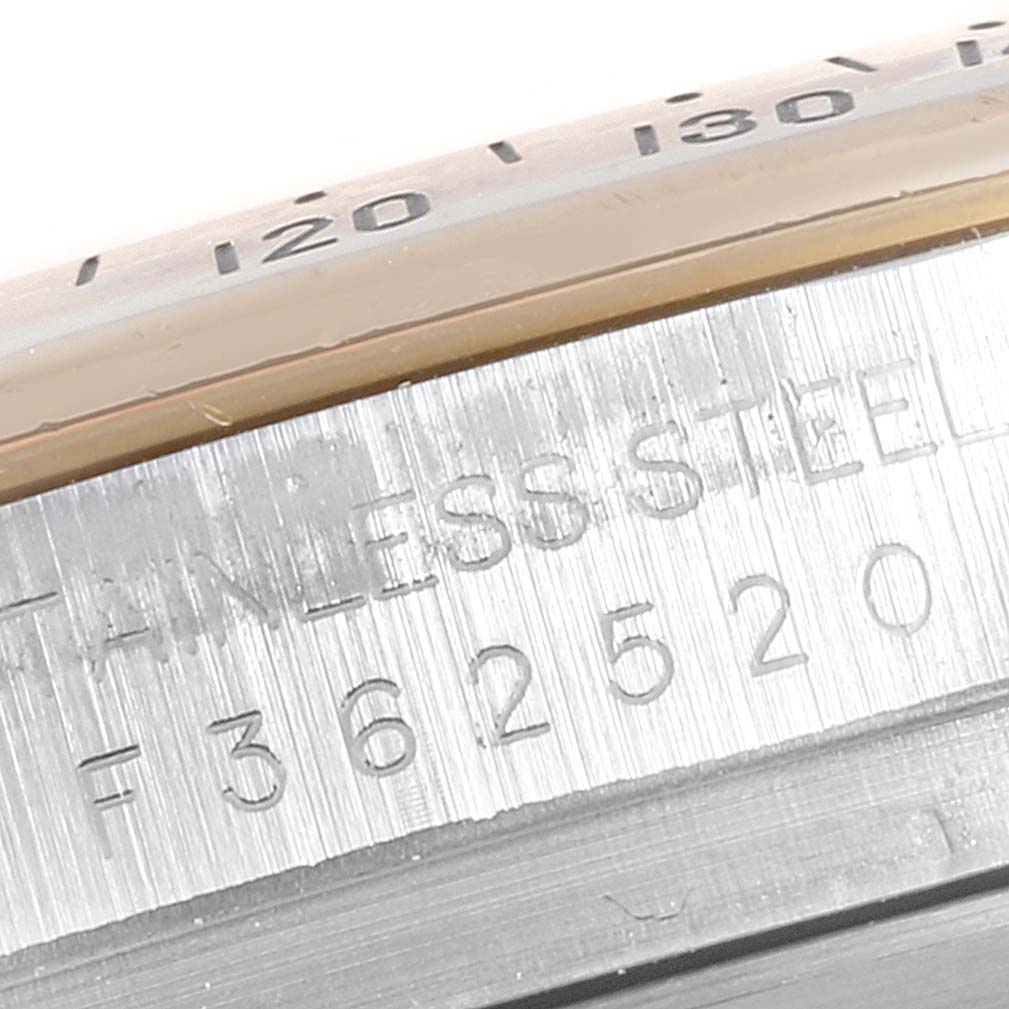 The image shows a close-up of the side of a Rolex Daytona 116523 Men
s Steel and Gold (two tone) Grey Dial 116523 Men
s Steel and Gold (two tone) Grey Dial watch, revealing part of the bezel and engraved model serial number.