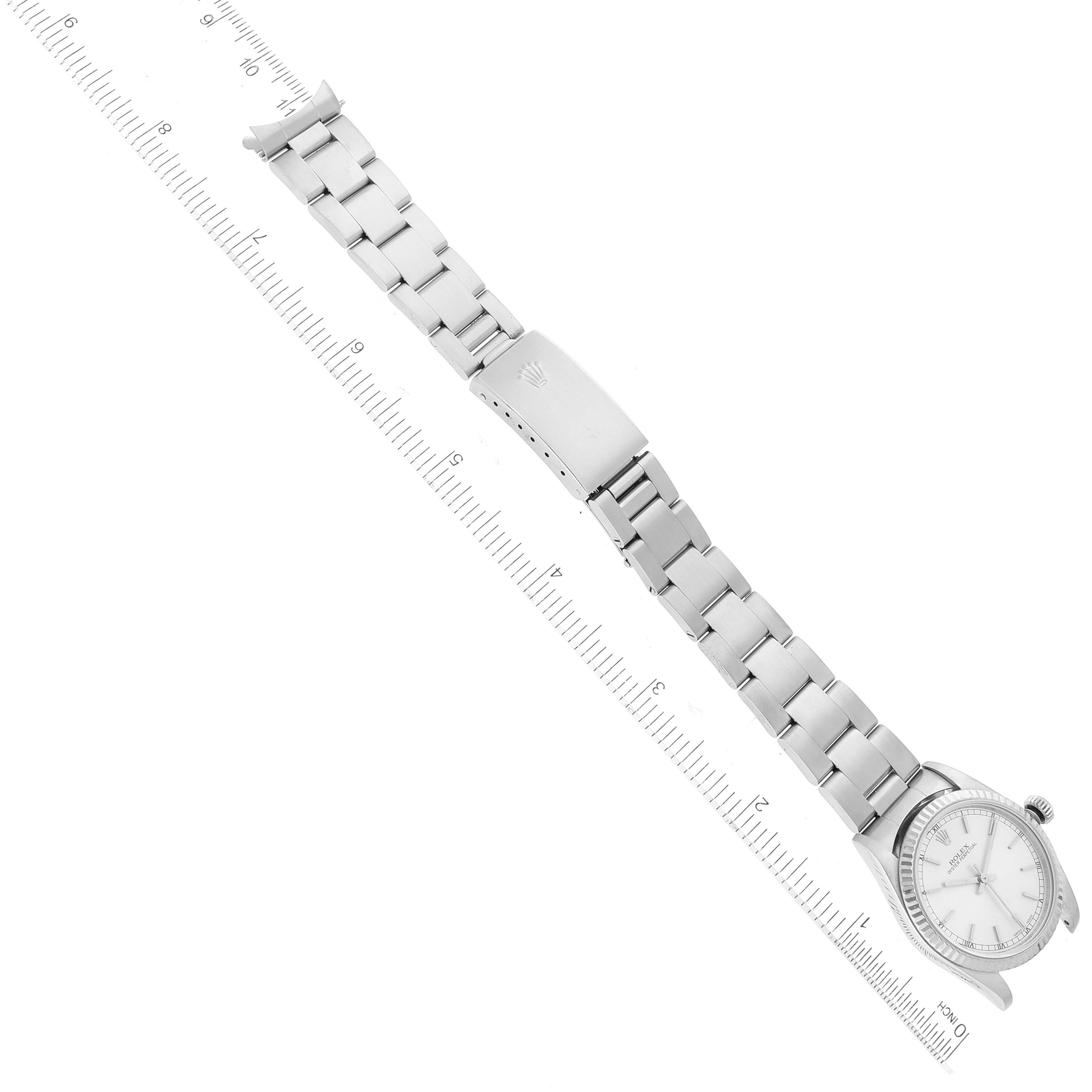This image shows an overhead view of a Rolex Mid-Size 77014 Women
s Stainless Steel Silver Dial 77014 Women
s Stainless Steel Silver Dial model, featuring its face, bracelet, and clasp, alongside a measuring ruler.