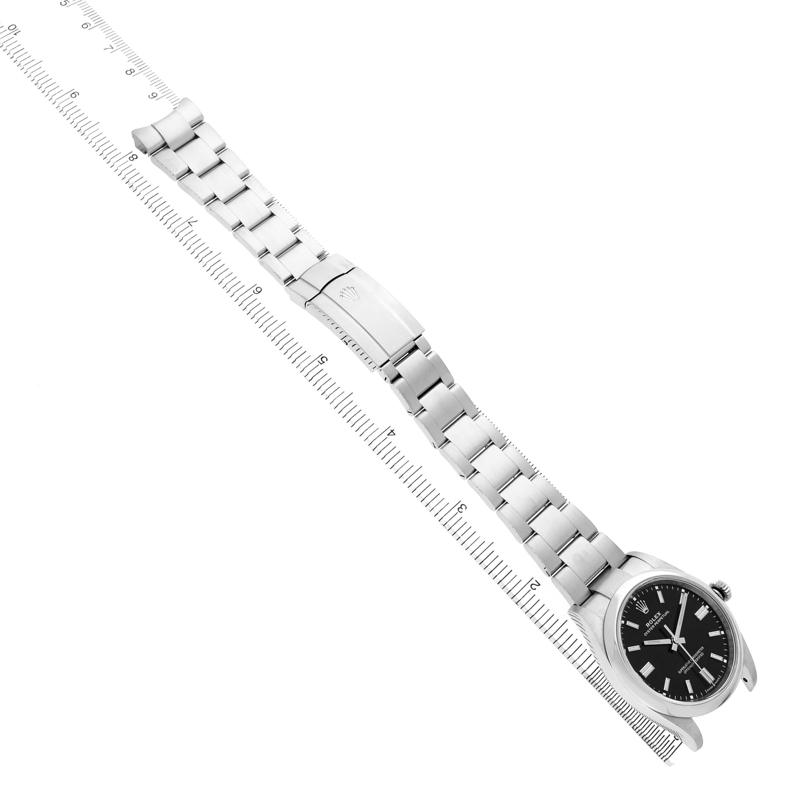 The Rolex Oyster Perpetual 126000 Men's Stainless Steel Black Dial watch is shown from a top angle, displaying its entire band, clasp, and face alongside a ruler.