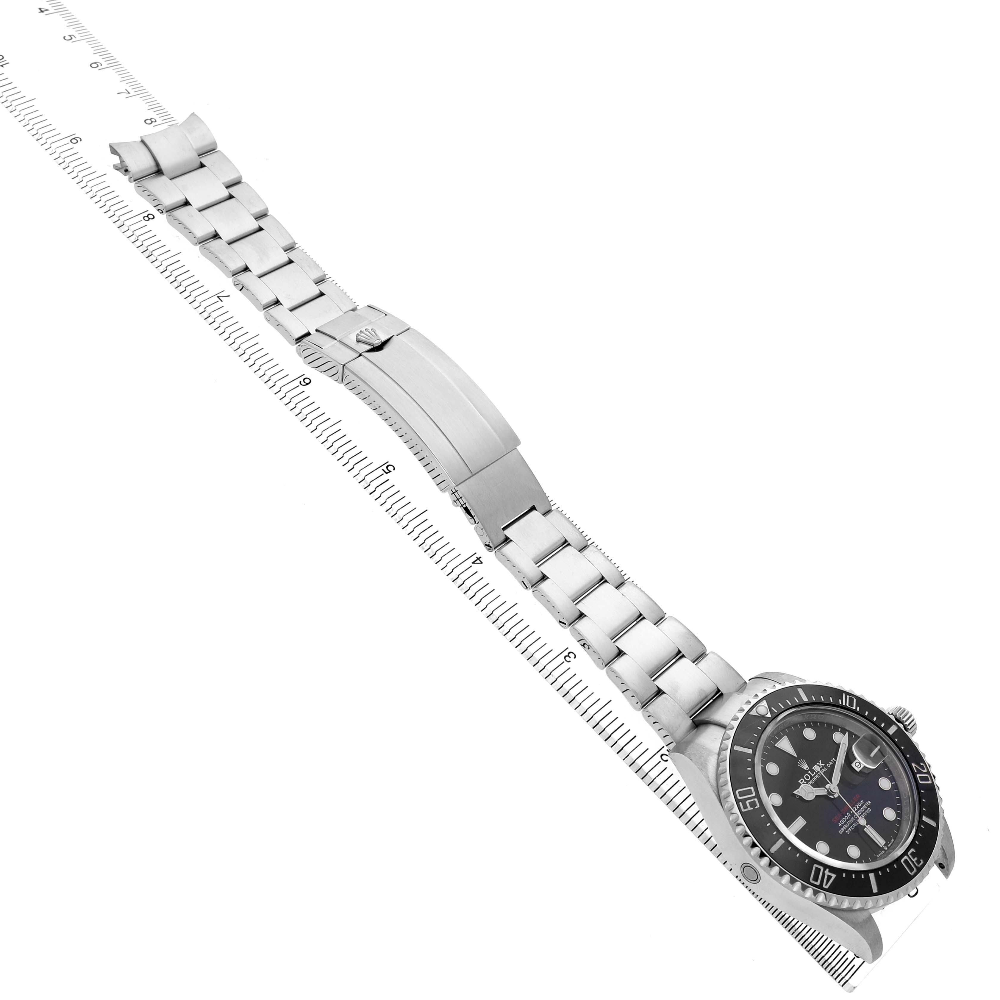 The Rolex Sea-Dweller 126600 Men's Stainless Steel Black Dial watch is shown laid flat, featuring the dial, bezel, bracelet, and clasp from a top-down angle next to a ruler.