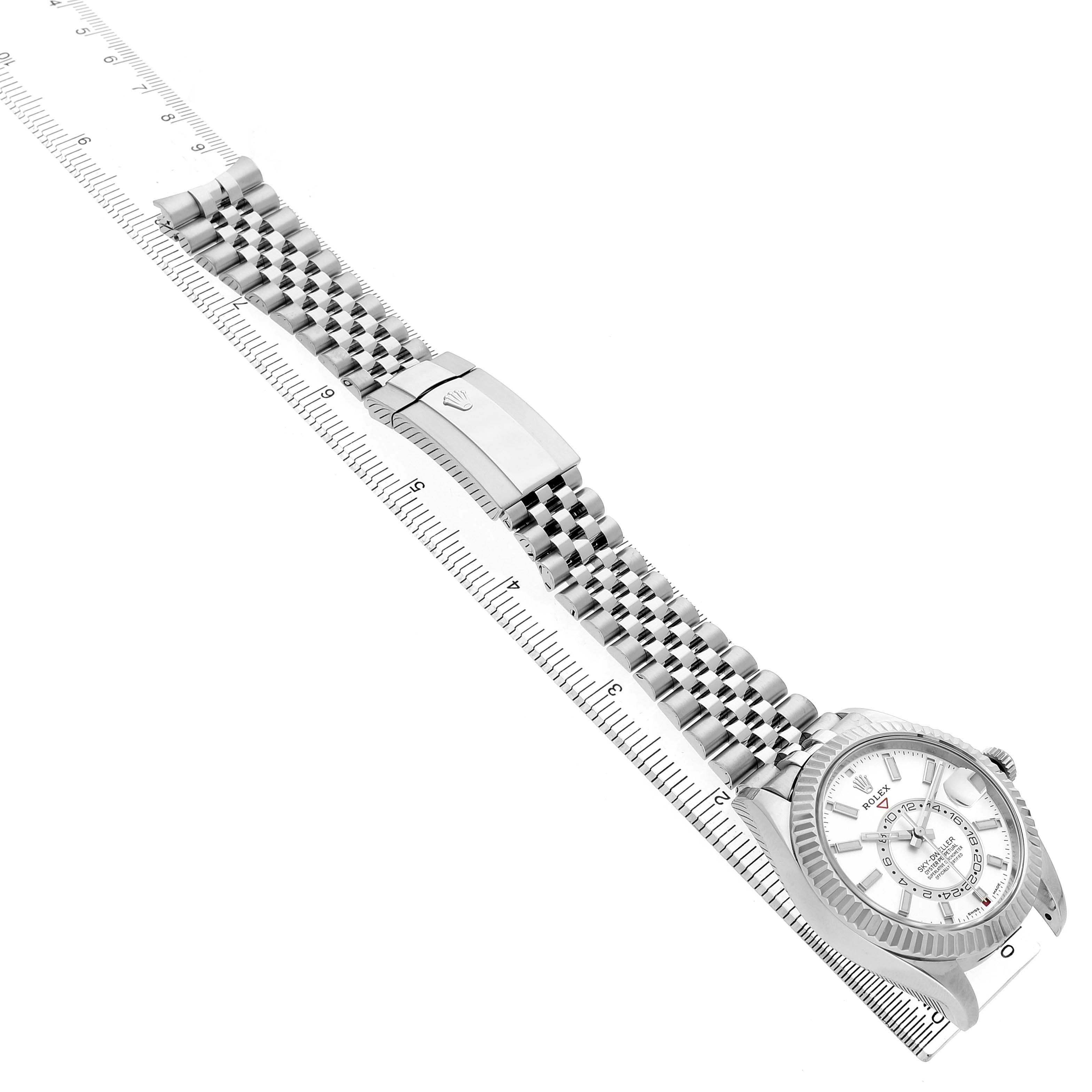 The Rolex Sky-Dweller 326934 Men's Stainless Steel Silver Dial watch is shown diagonally, highlighting its bracelet, clasp, and partially visible face with a ruler beside it.