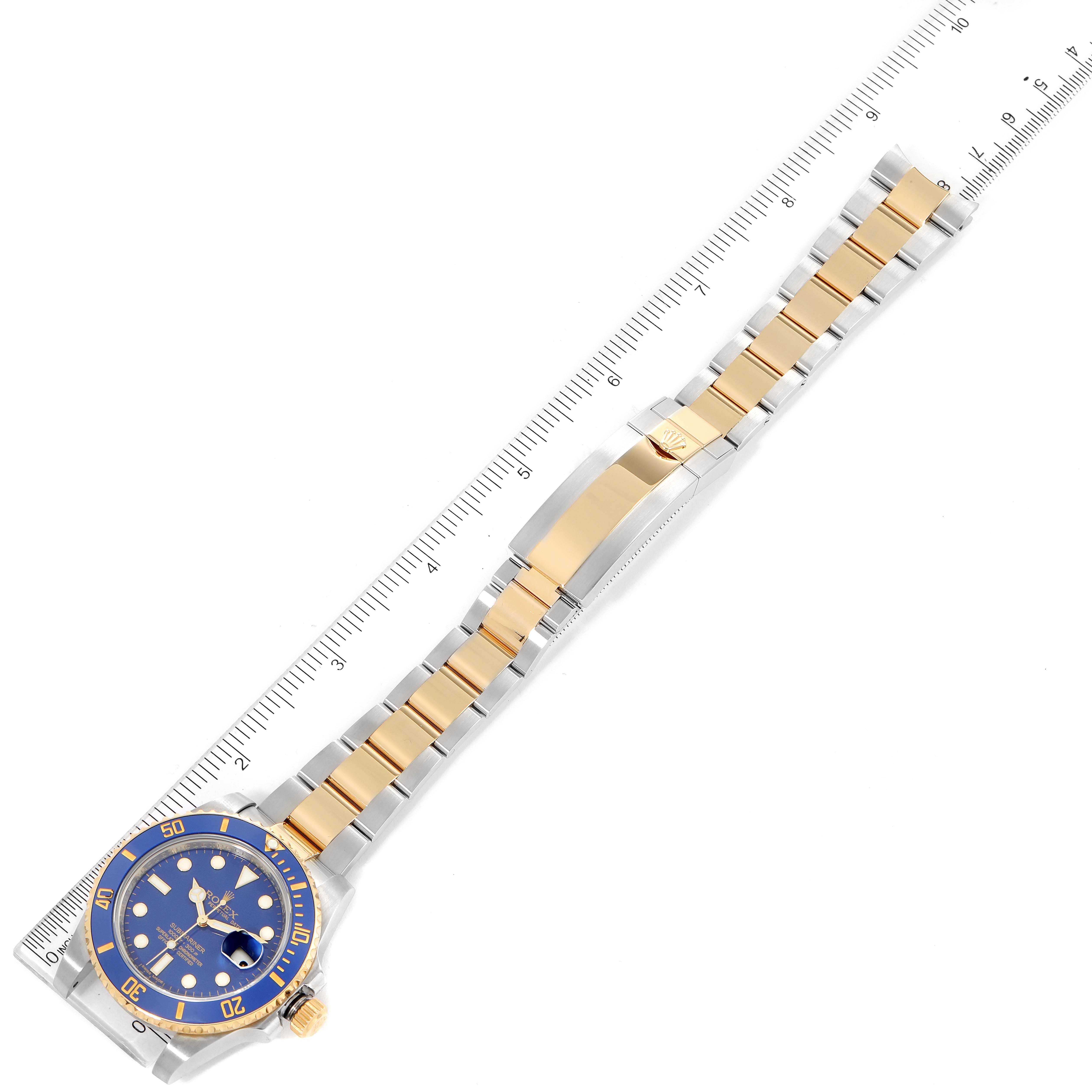 The image shows a Rolex Submariner 116613 Men
s Steel and Gold (two tone) Blue Dial 116613 Men
s Steel and Gold (two tone) Blue Dial watch laid flat alongside a ruler, displaying the entire watch face and band.