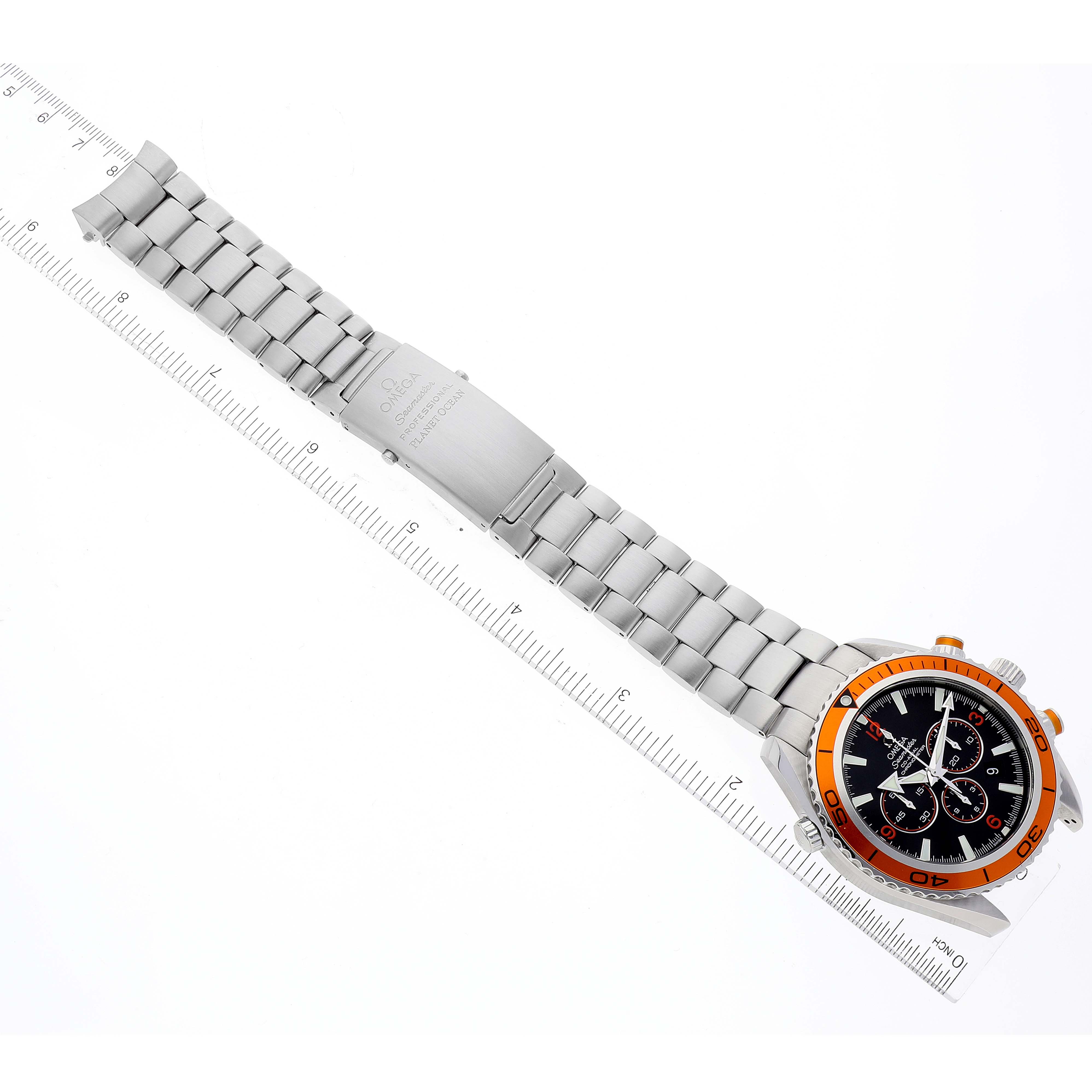 The image shows an Omega Planet Ocean 2218.50.00 Men
s Stainless Steel Black Dial 2218.50.00 Men
s Stainless Steel Black Dial watch at an angle, displaying the watch face, bracelet, and clasp alongside a ruler for scale.