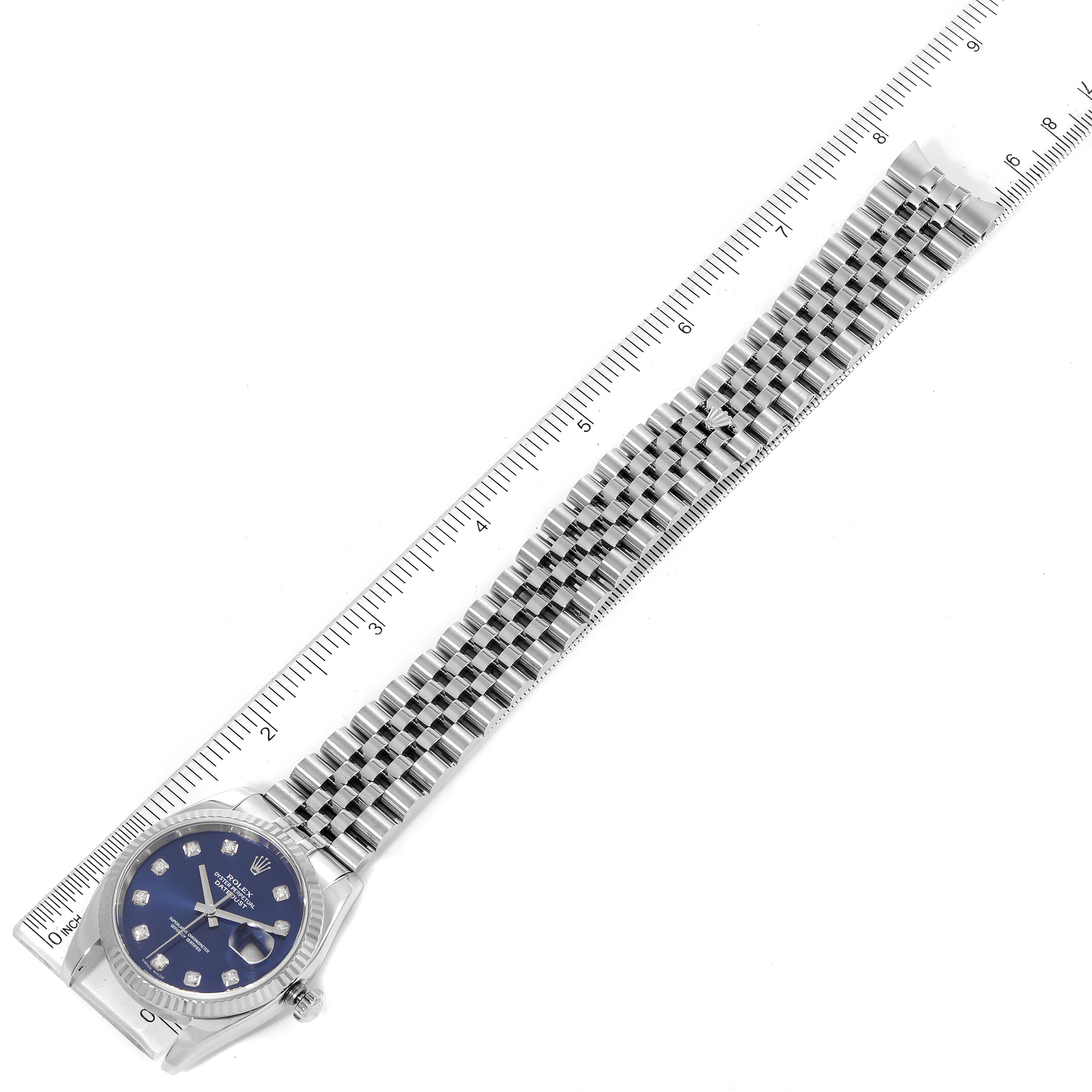 The image shows a top view of a Rolex Datejust 116234 Men's Stainless Steel Blue Dial 116234 Men's Stainless Steel Blue Dial watch with a blue dial and jubilee bracelet alongside a ruler for scale.
