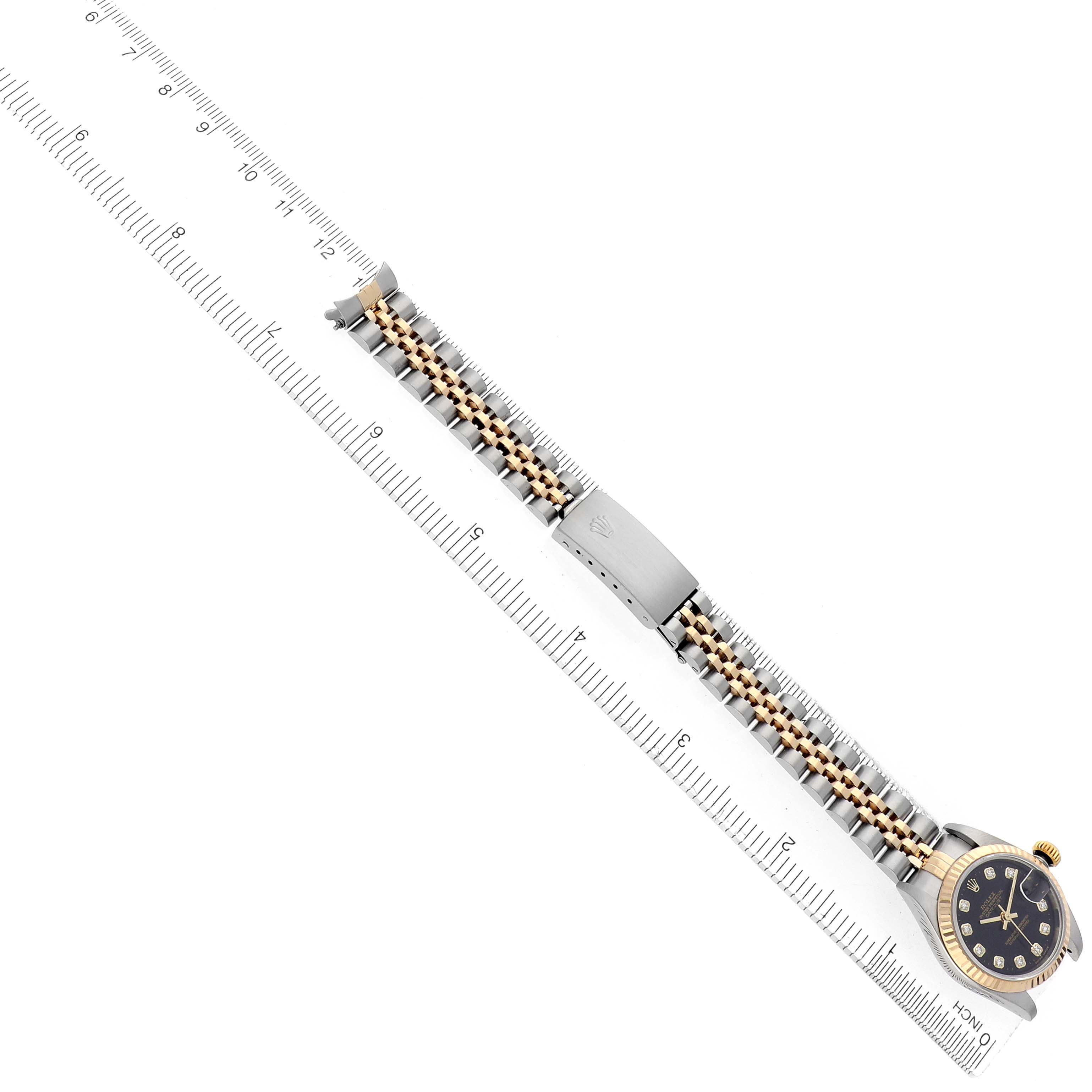 The Rolex Datejust 79173 Women
s Steel and Gold (two tone) Black Dial 79173 Women
s Steel and Gold (two tone) Black Dial watch is shown from a top-down angle, highlighting the bracelet, clasp, and face alongside a ruler for scale.