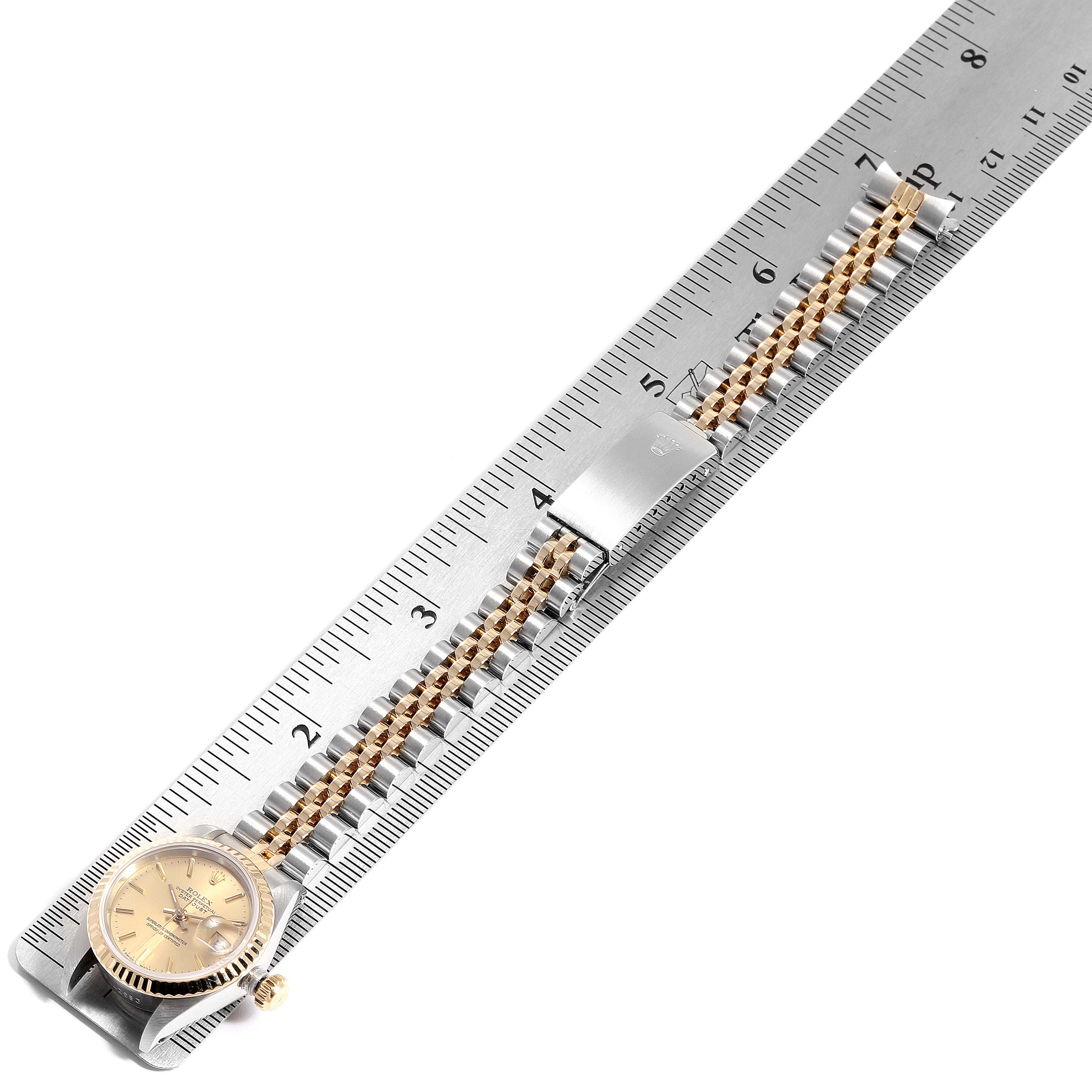 The image shows a Rolex Datejust 69173 Women
s Steel and Gold (two tone) Champagne Dial 69173 Women
s Steel and Gold (two tone) Champagne Dial watch from a top-down angle, highlighting the face and metal bracelet placed alongside a ruler.