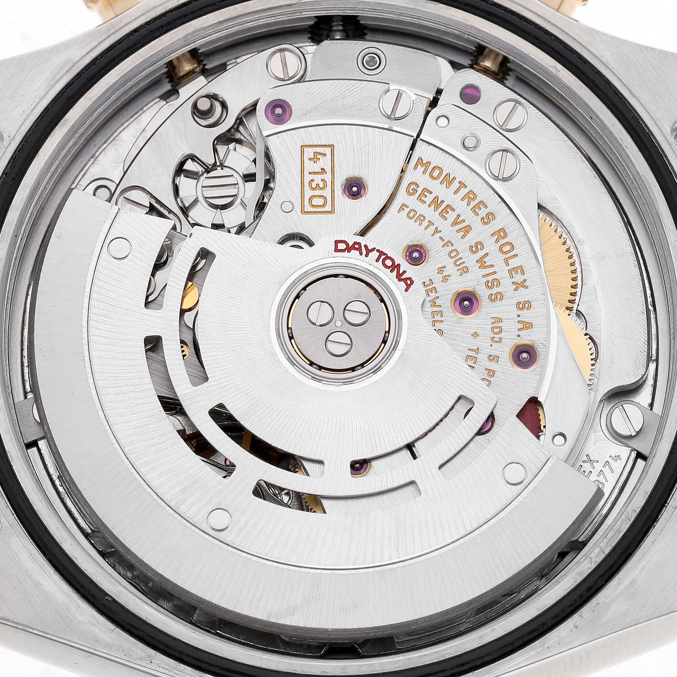 The image shows a close-up of the movement mechanism inside a Rolex Daytona 116523 Men's Stainless Steel White Dial watch, highlighting gears and engravings.