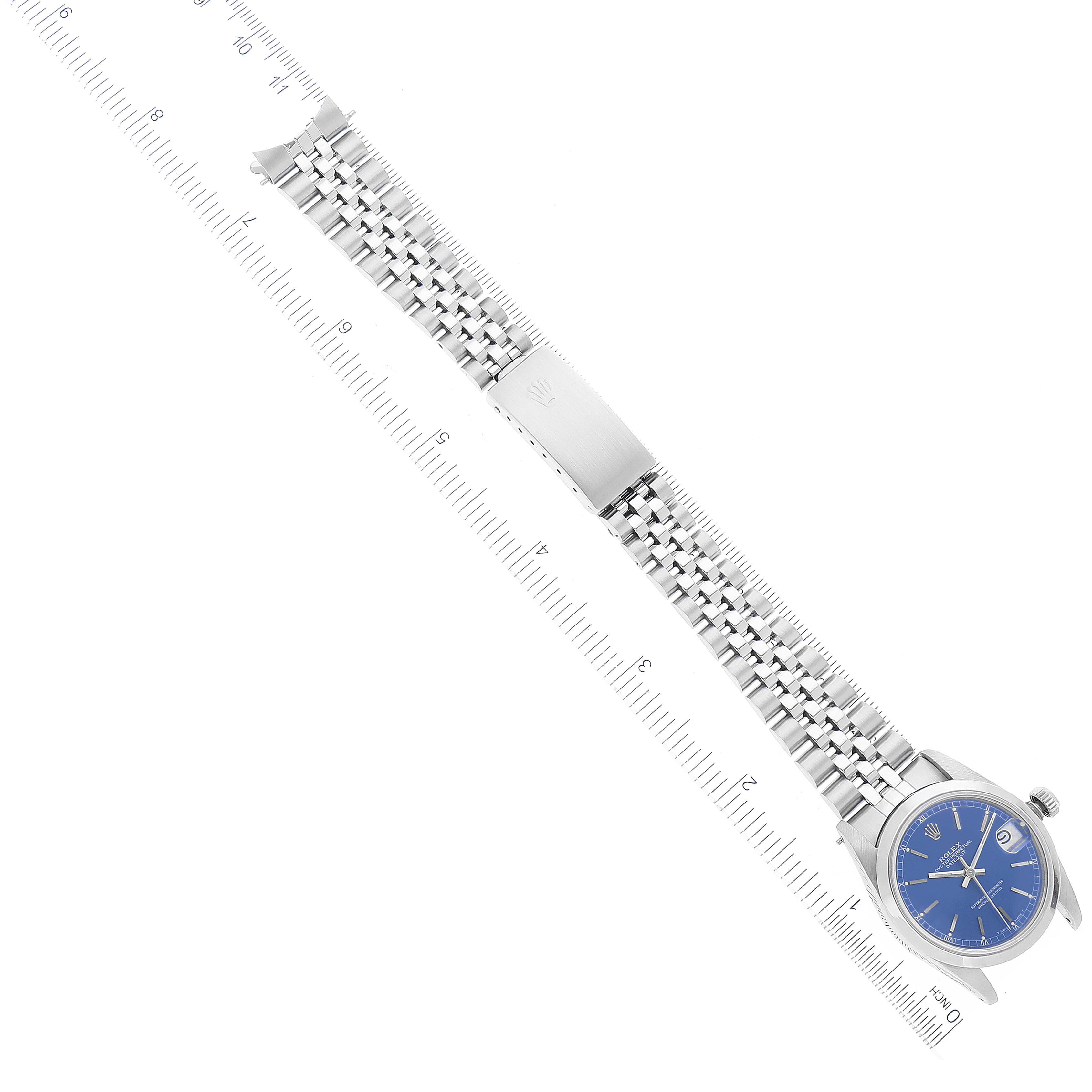 The image shows a Rolex Mid-Size 68240 Women
s Stainless Steel Blue Dial 68240 Women
s Stainless Steel Blue Dial watch laid flat with a visible blue dial, silver bracelet, and clasp, alongside a ruler for scale.