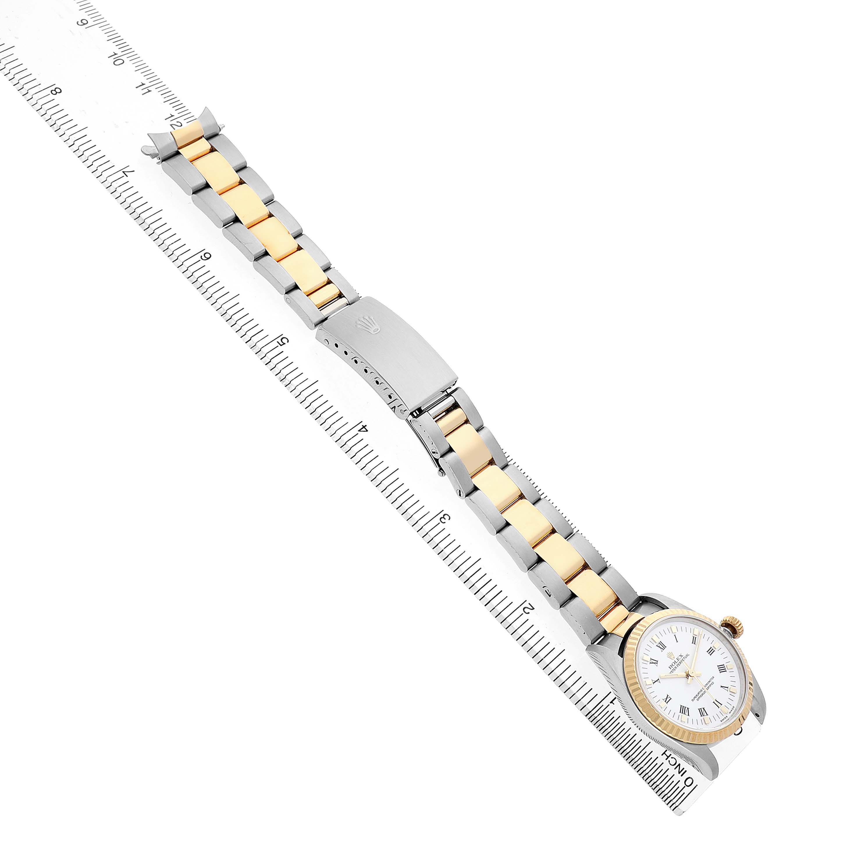 The Rolex Oyster Perpetual 67513 Women's Steel and Gold (two tone) White Dial watch is shown at an angle highlighting its two-tone bracelet and clasp alongside a ruler.