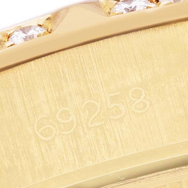 The image shows a close-up of the Rolex President 69258 Women's Yellow Gold White Dial model's gold case with a partial view of its bezel and engraved model number.