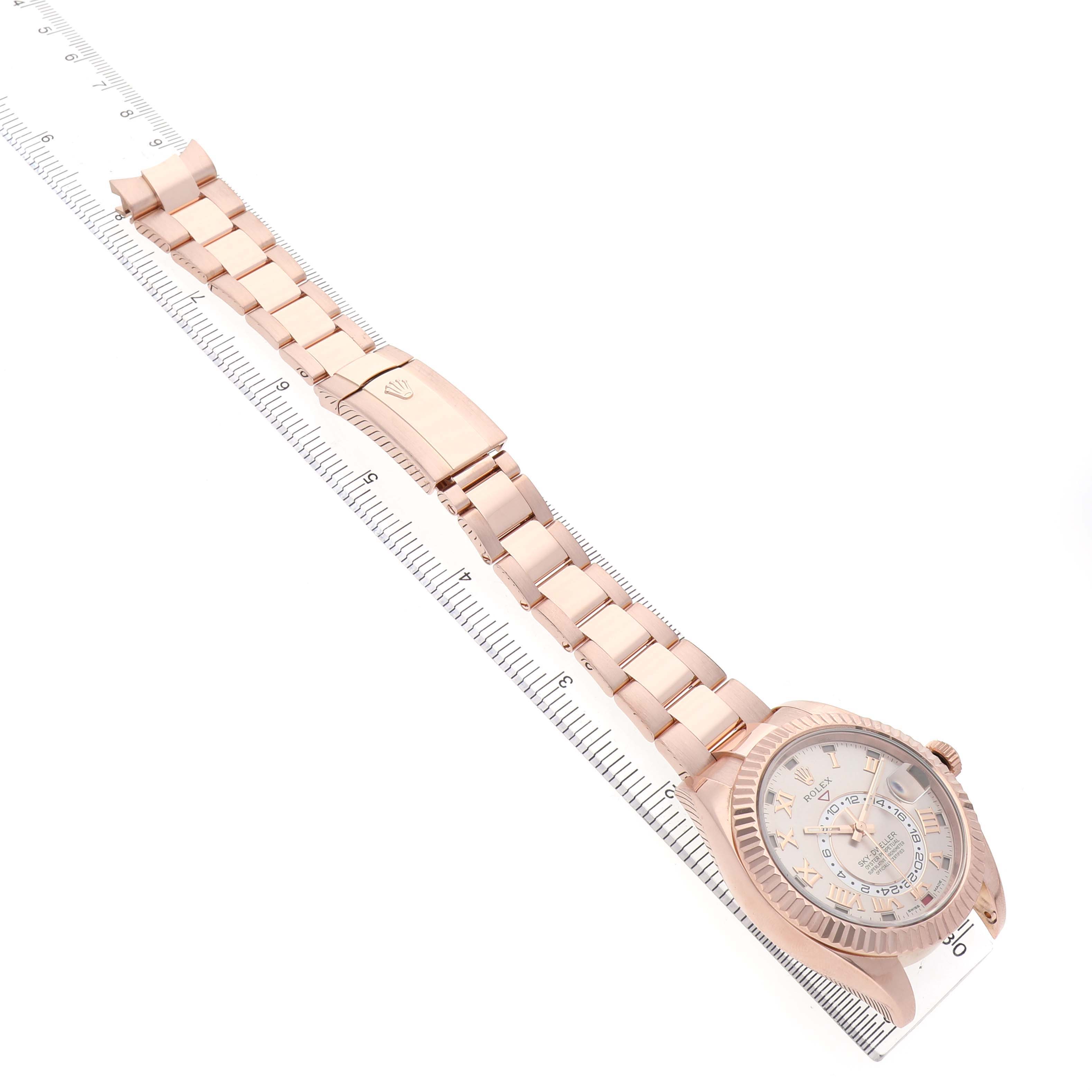The Rolex Sky-Dweller 326935 Men's Rose Gold Pink Dial is shown from an angled top view, featuring the full bracelet and the watch face, aligned with a ruler.