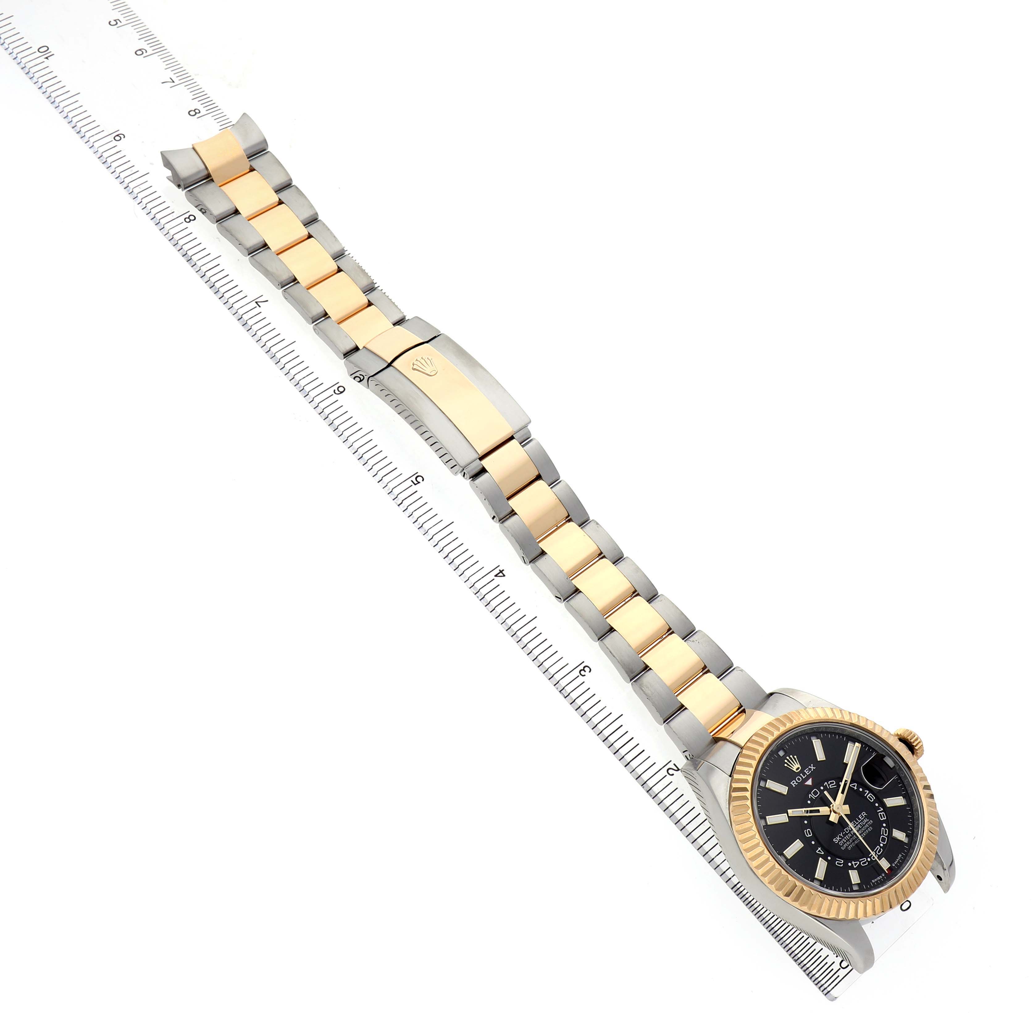 The Rolex Sky-Dweller 336933 Men's Steel and Gold (two tone) Black Dial watch is shown at an oblique top view, highlighting the gold bezel, black dial, and two-tone bracelet aligned with a ruler.