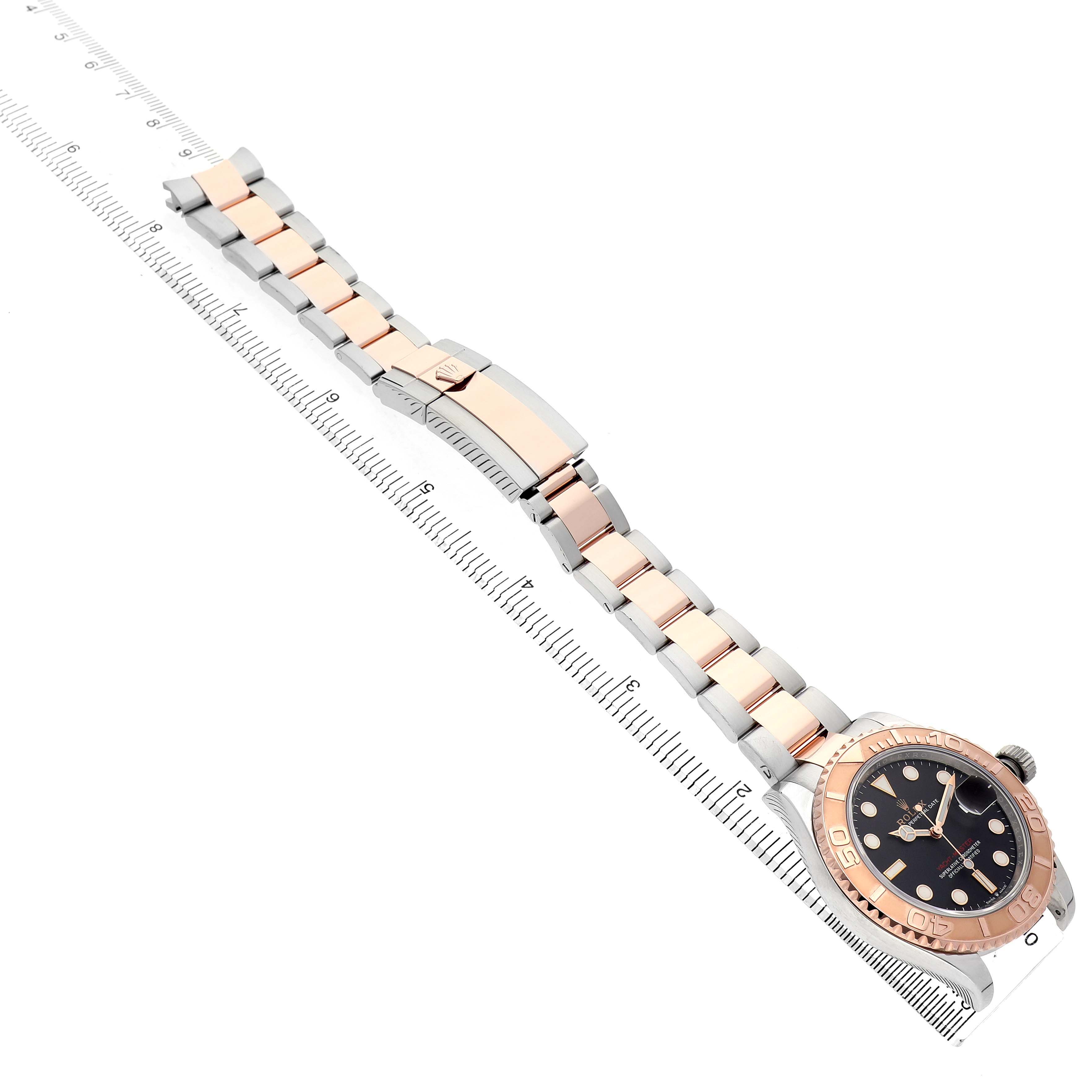 The Rolex Yacht-Master 126621 Men's Stainless Steel Black Dial watch is shown from an overhead angle, highlighting its rose gold and steel bracelet alongside a ruler.