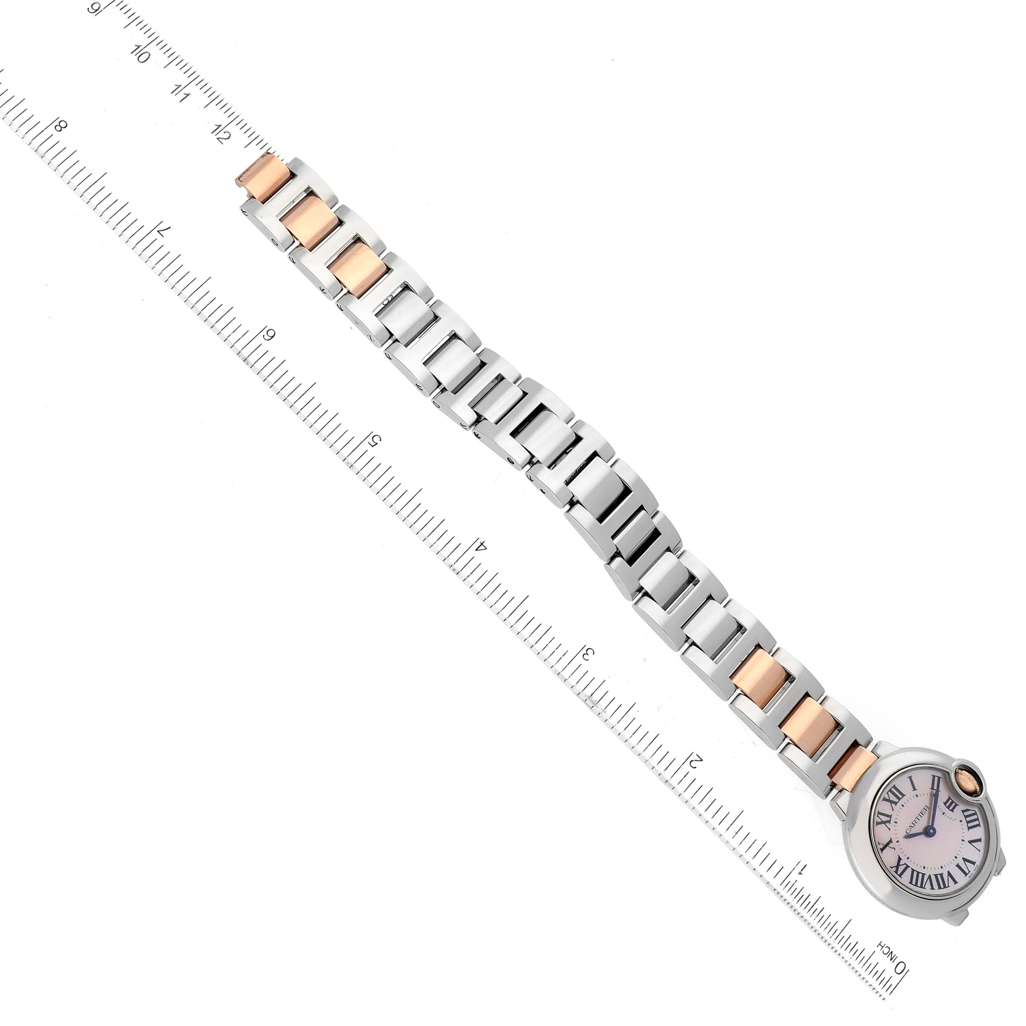 The image shows a Cartier Ballon Bleu W6920034 Women's Steel and Gold (two tone) Mother of Pearl Dial W6920034 Women's Steel and Gold (two tone) Mother of Pearl Dial watch at an angle, featuring its face and segmented metal bracelet placed along a ruler.