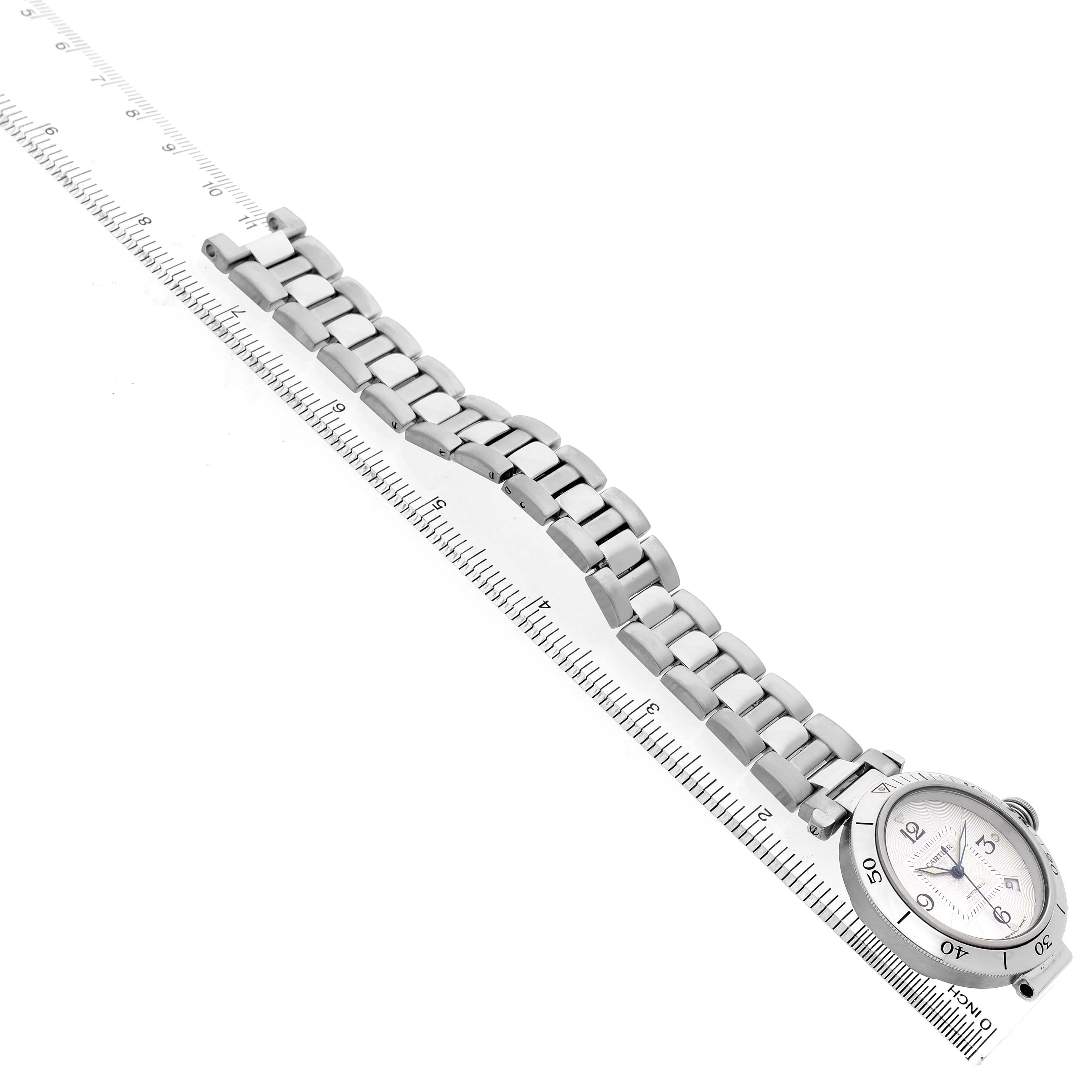 The image shows a side angle of the Cartier Pasha W31059H3 Men's Stainless Steel Silver Dial watch, highlighting its bracelet and dial alongside a ruler.